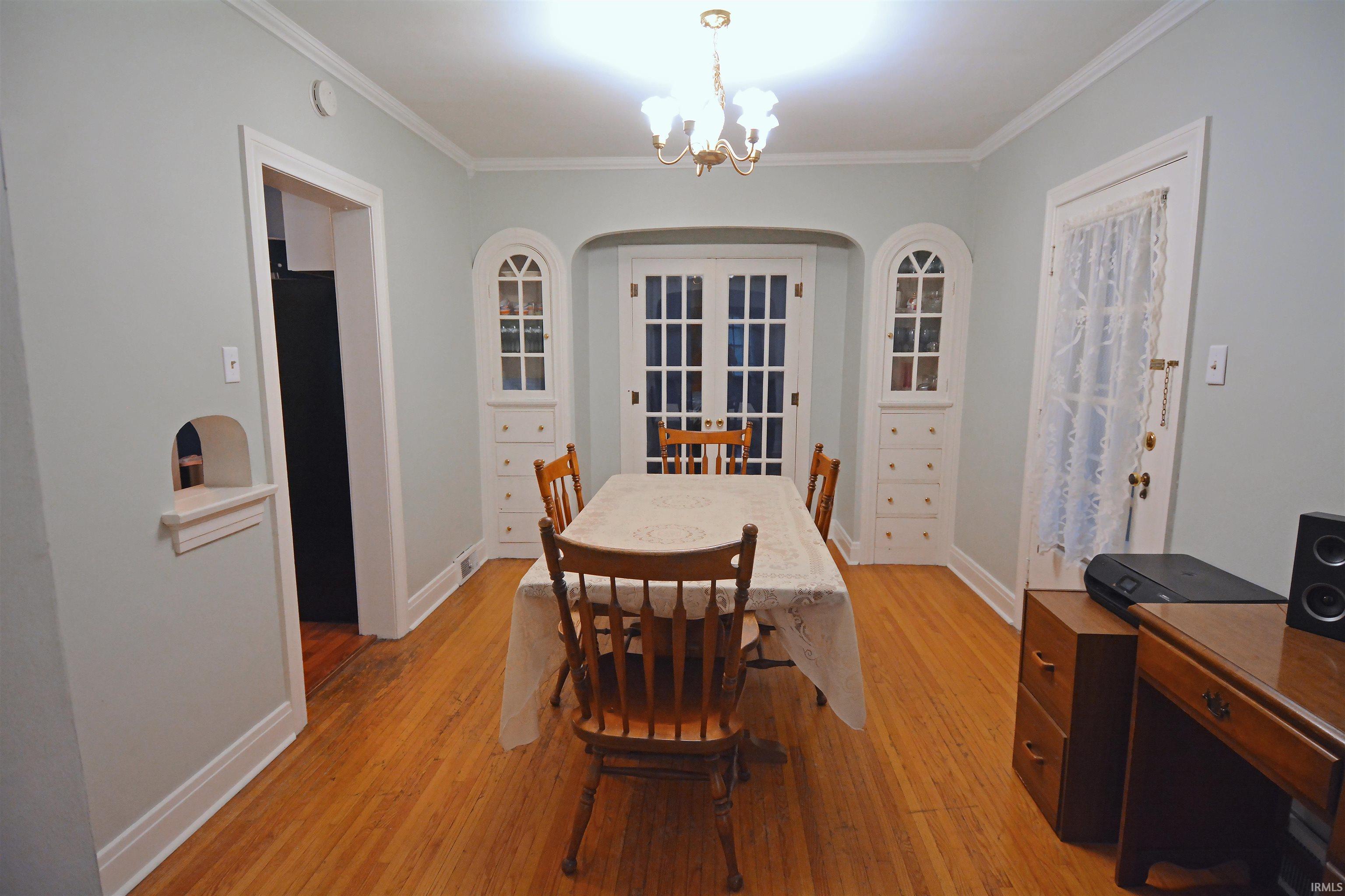 Dining area featuring wood-finish flooring, crown molding, and a chandelier