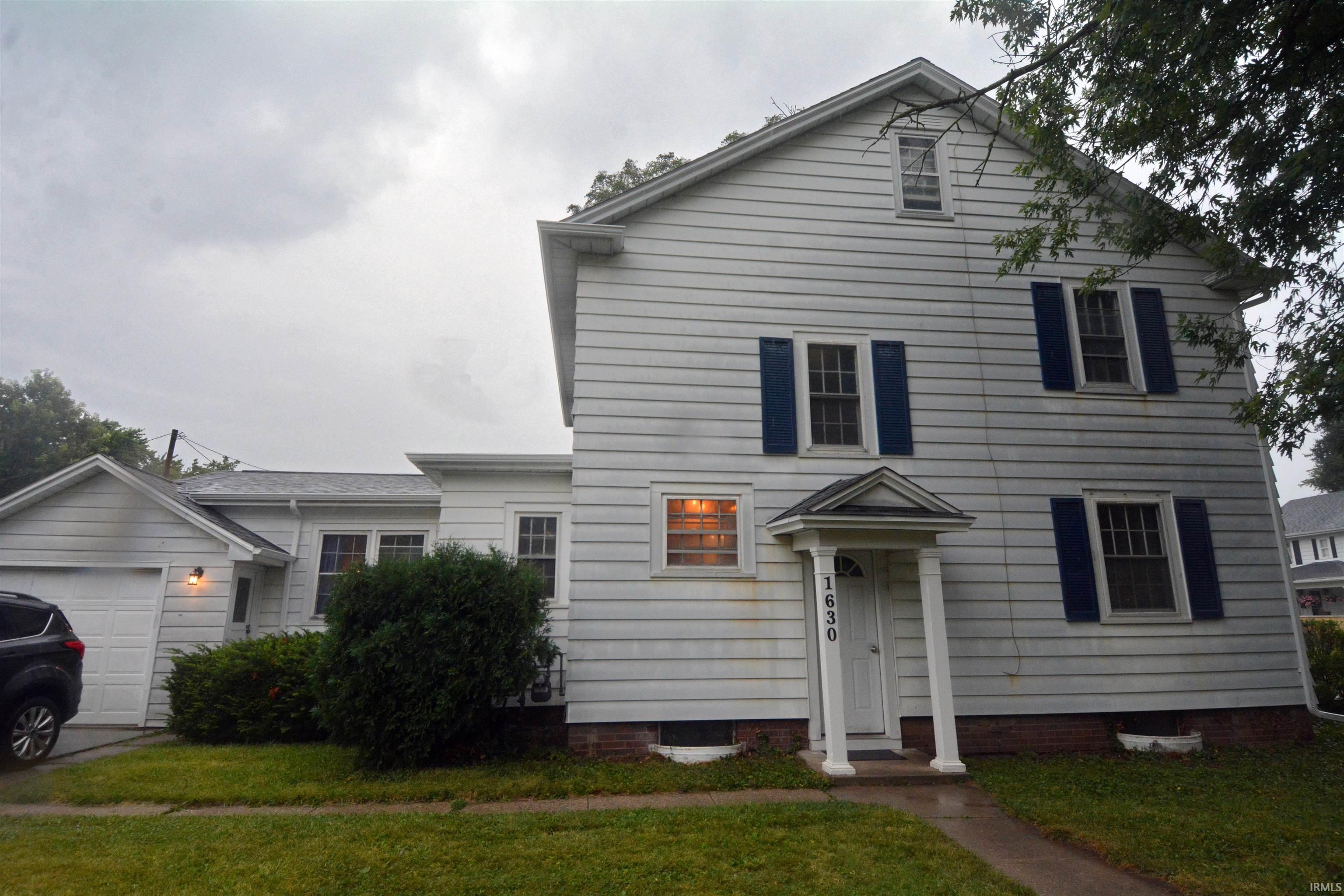 Traditional siding exterior featuring blue window shutters, a covered entry with columns, and an attached single-car garage