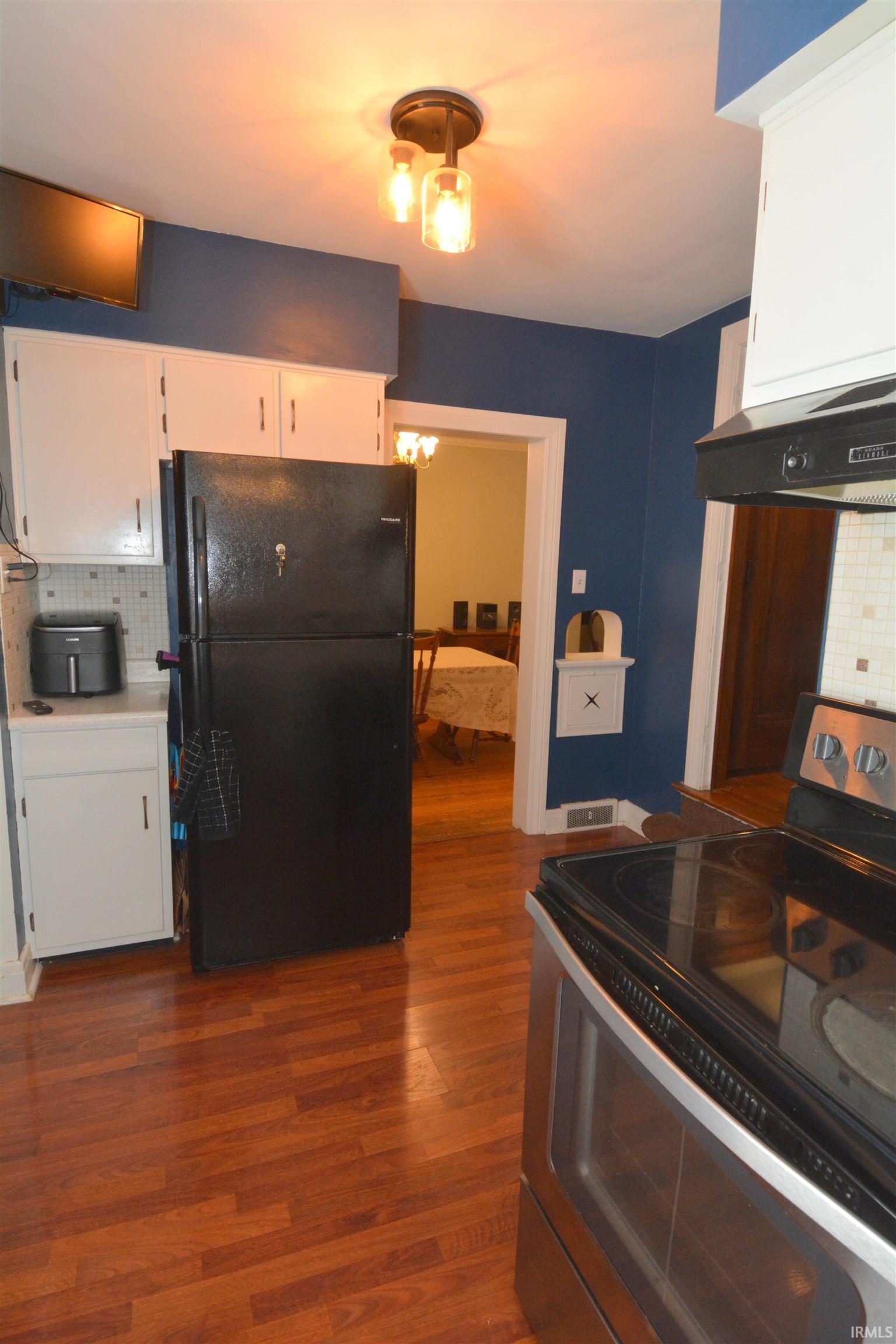 Kitchen featuring wood-finish flooring, white cabinetry, a black refrigerator, a stainless steel range, and a two-bulb ceiling light fixture