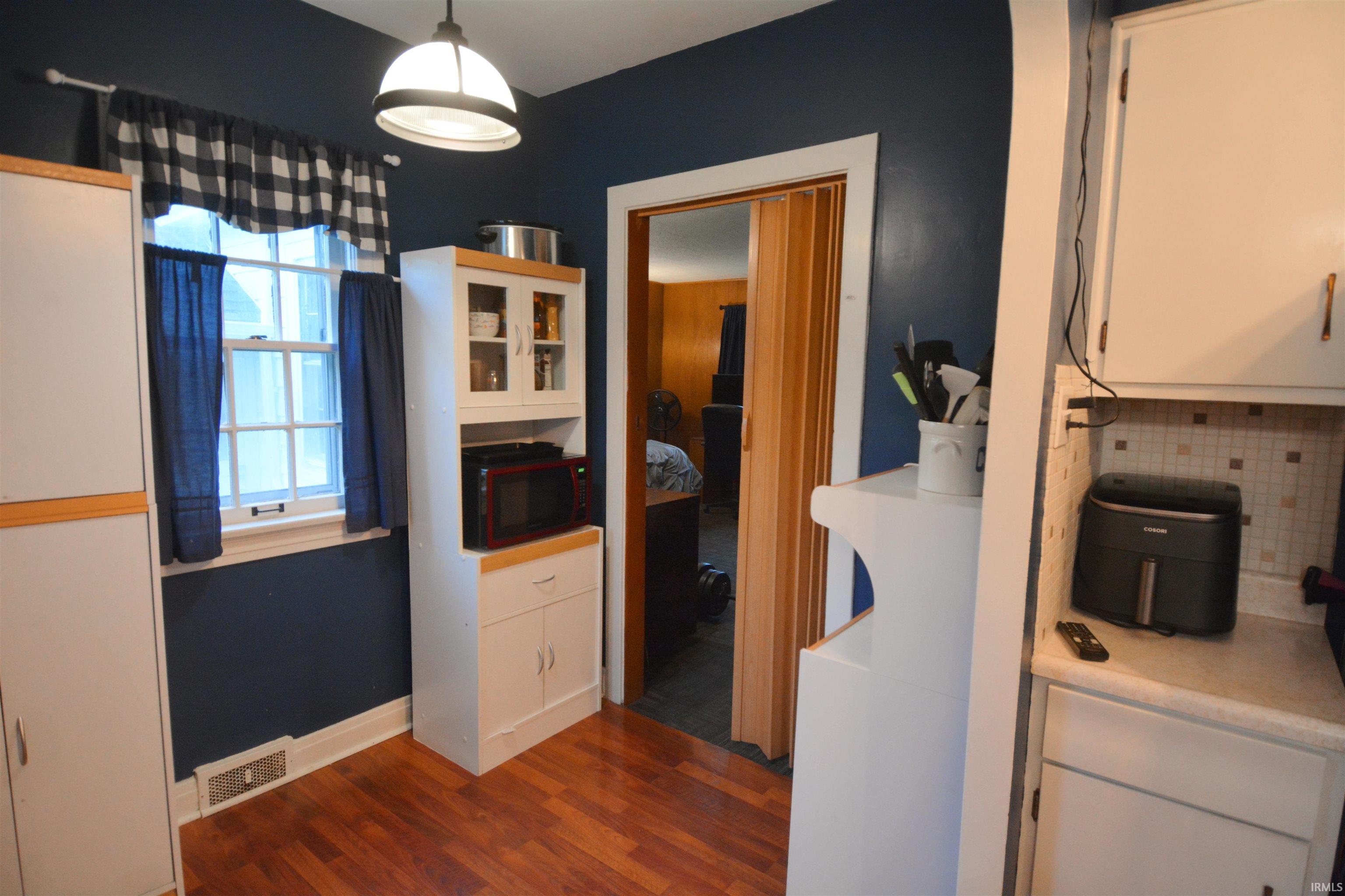 Kitchen area with wood-finish flooring, white cabinetry, and a white tile backsplash