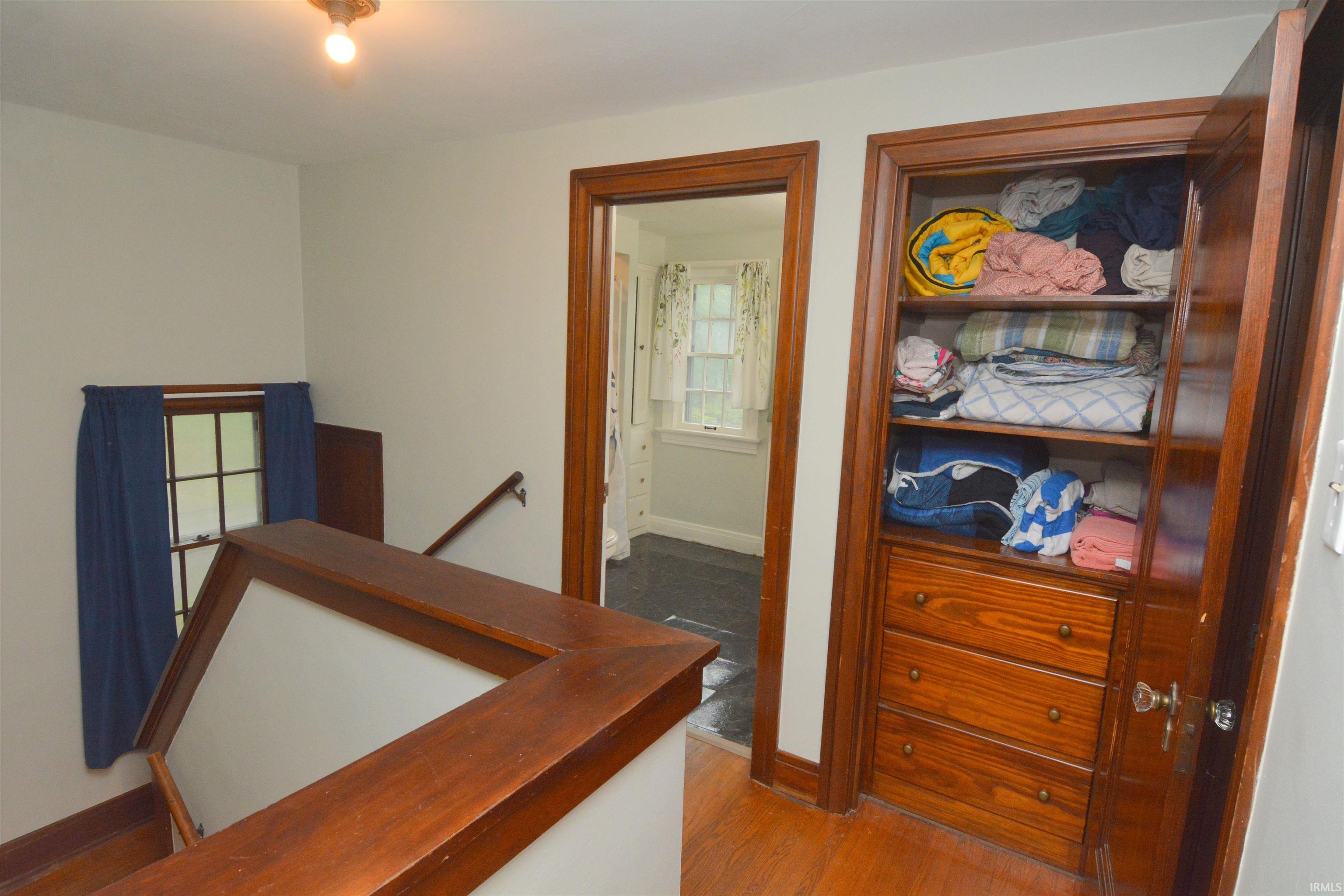 Built-in linen closet with wood shelving and three wood drawers, complemented by a wood-trimmed doorway and wood flooring