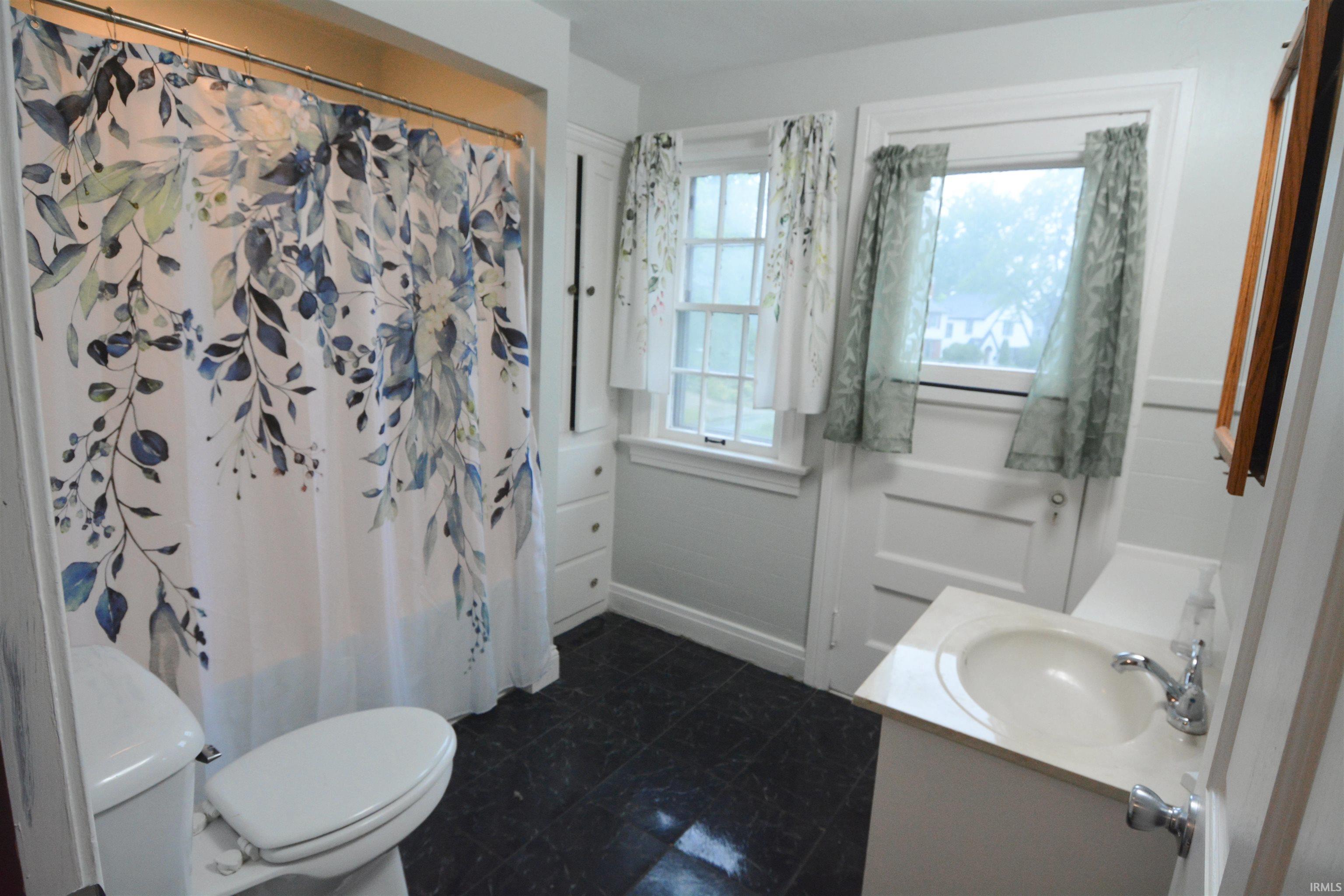 Bathroom featuring dark tile flooring, a white vanity with an integrated sink, a commode, and a built-in storage cabinet with drawers