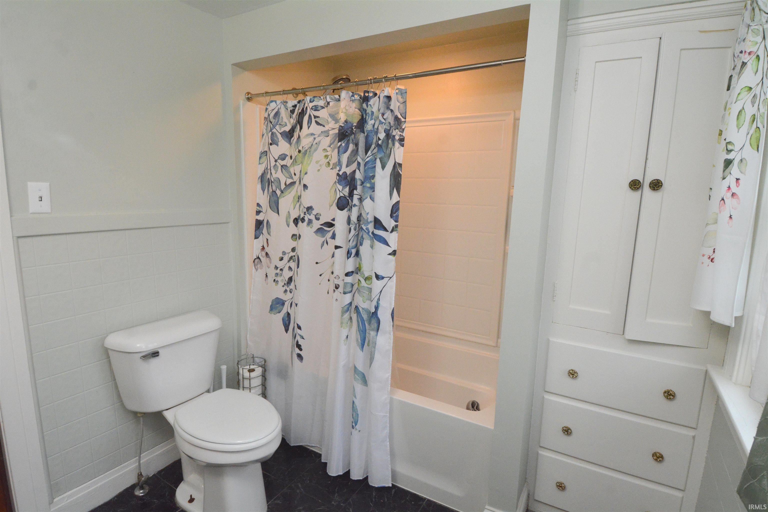 Bathroom featuring a full tub and shower combination, white toilet, built-in storage cabinetry with two upper doors, and three lower drawers