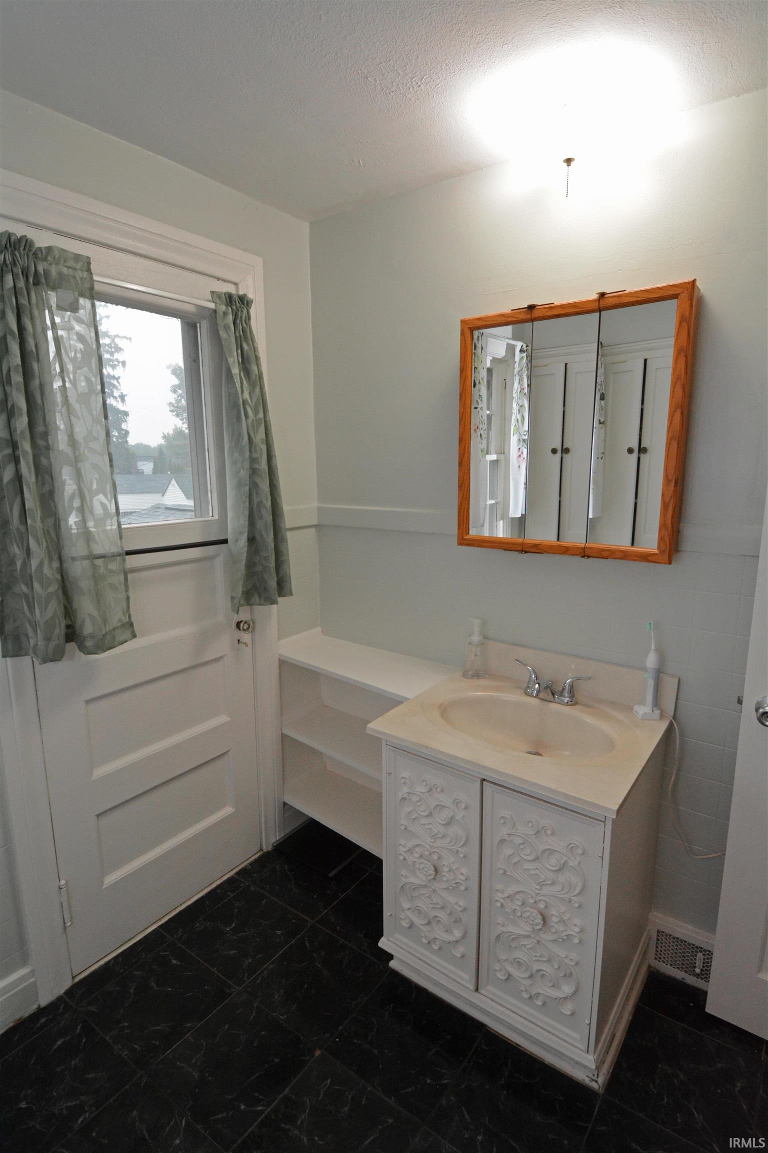 Bathroom featuring a vanity with an integrated sink, a framed medicine cabinet, built-in shelving, and dark-toned floor tiles