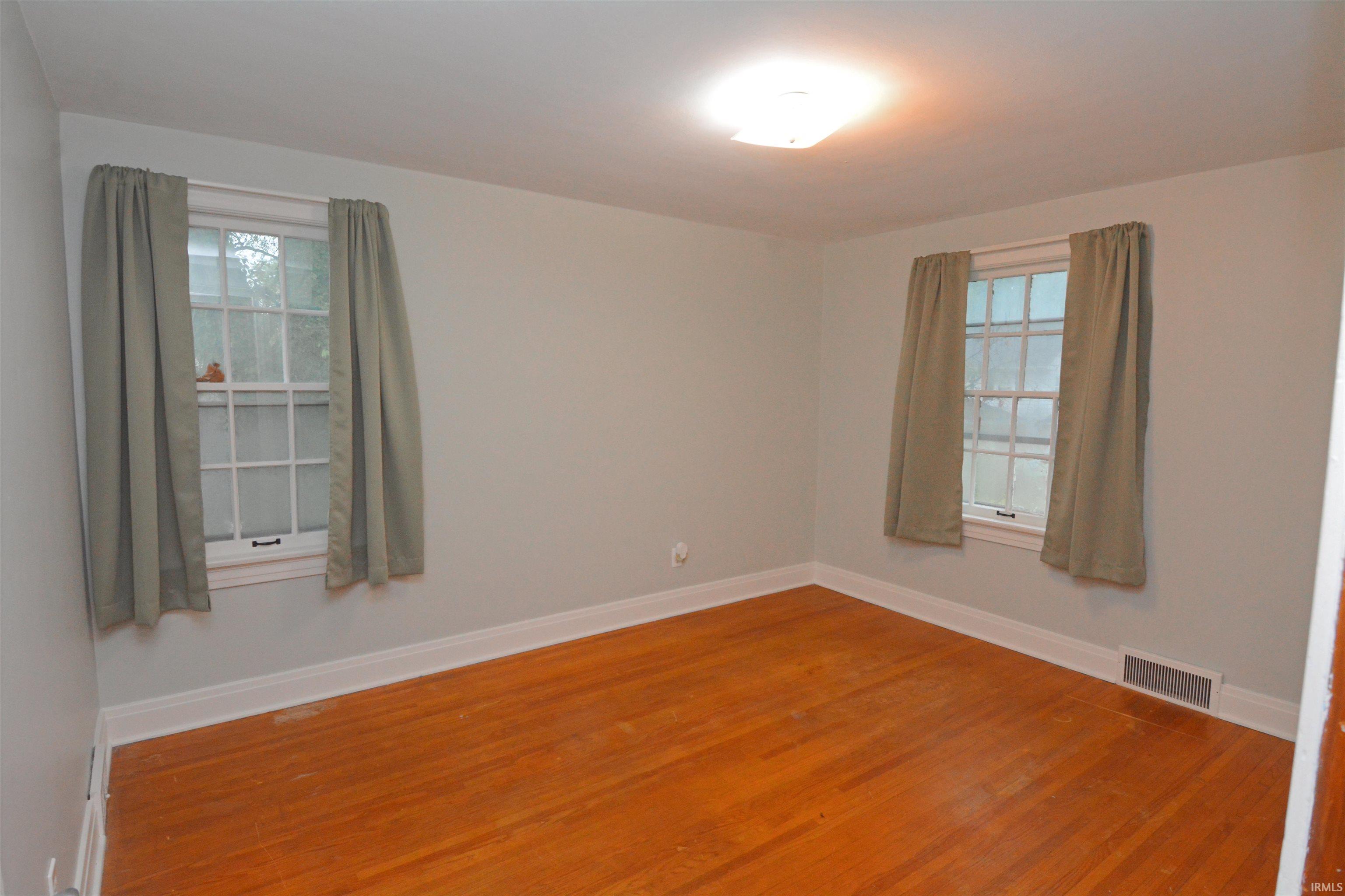 Hardwood flooring with white baseboards, two double-hung windows, and a flush mount ceiling light fixture