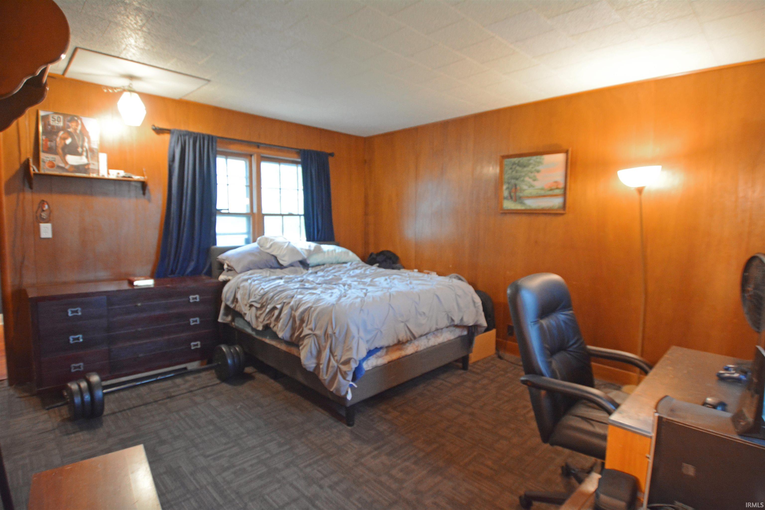 Room featuring wood-paneled walls, carpet flooring, a multi-pane window with dark drapes, and a ceiling-mounted light fixture