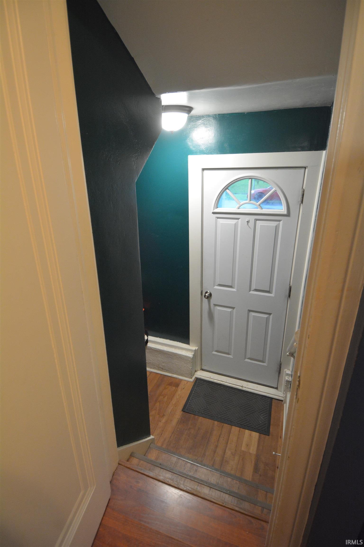 Entryway featuring a white paneled door with an arched stained-glass insert, wood-finish flooring, and a flush-mount ceiling light fixture