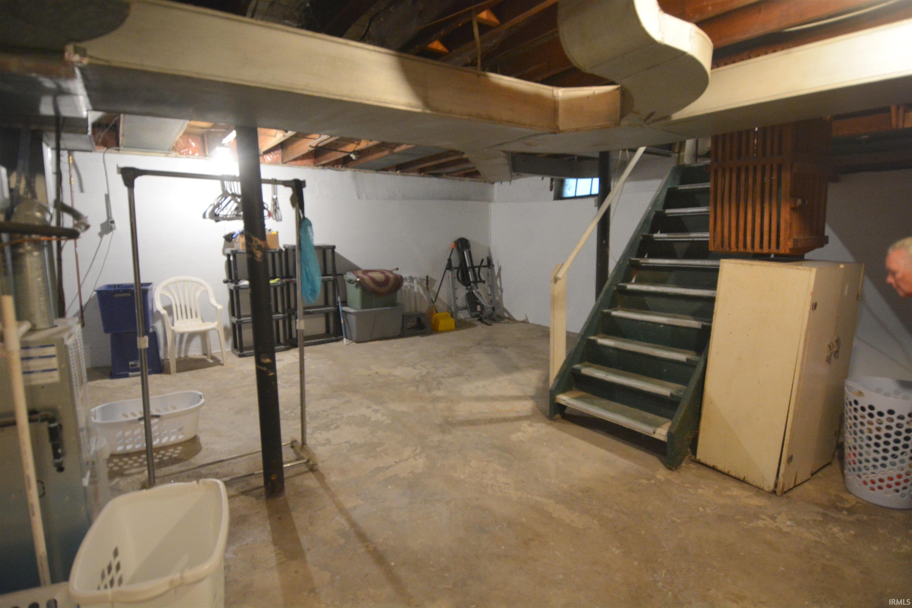 Expansive basement space featuring exposed ceiling joists, concrete flooring, and a painted wooden staircase