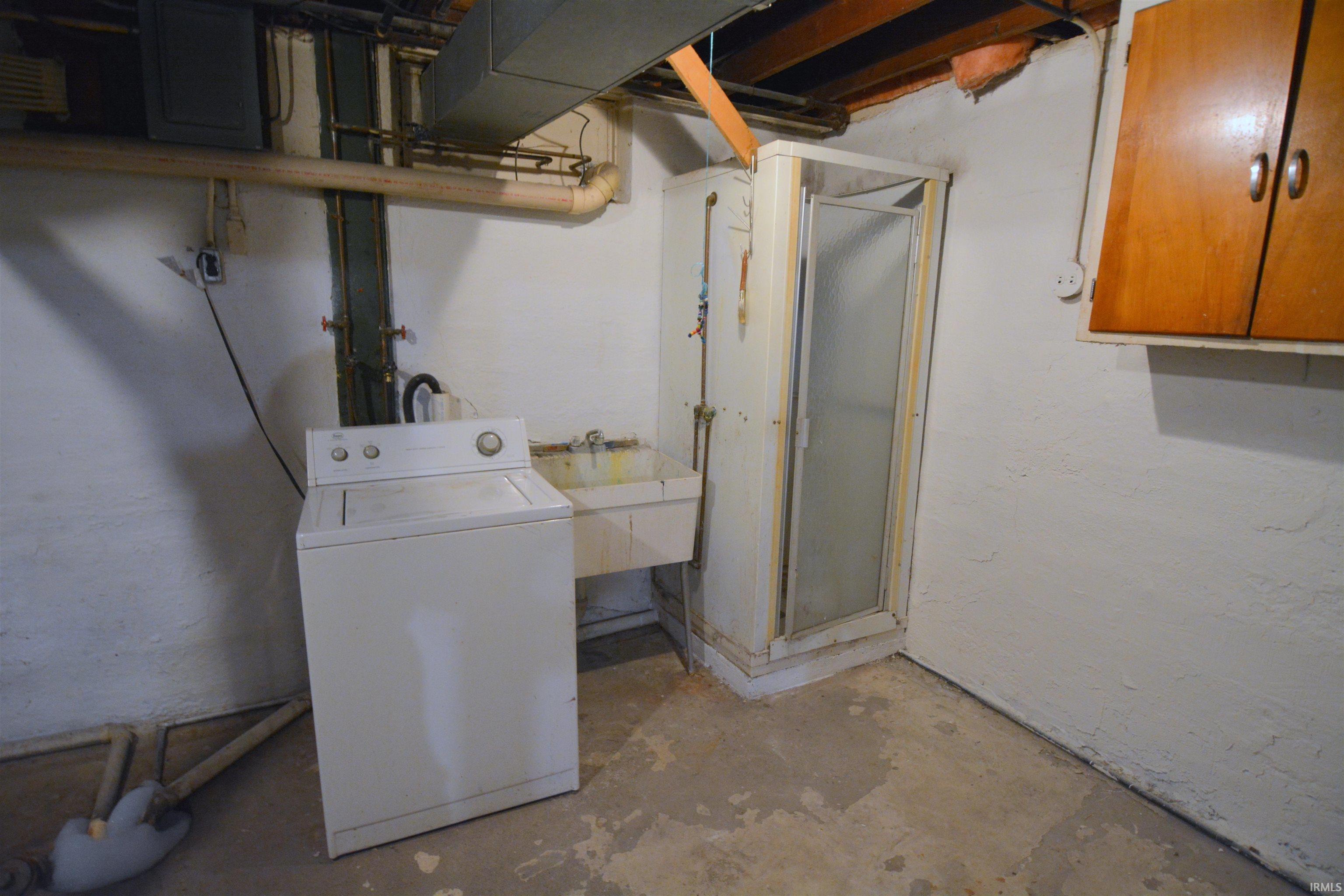 Utility area featuring a standalone shower enclosure, a utility sink, and wall-mounted wooden cabinetry