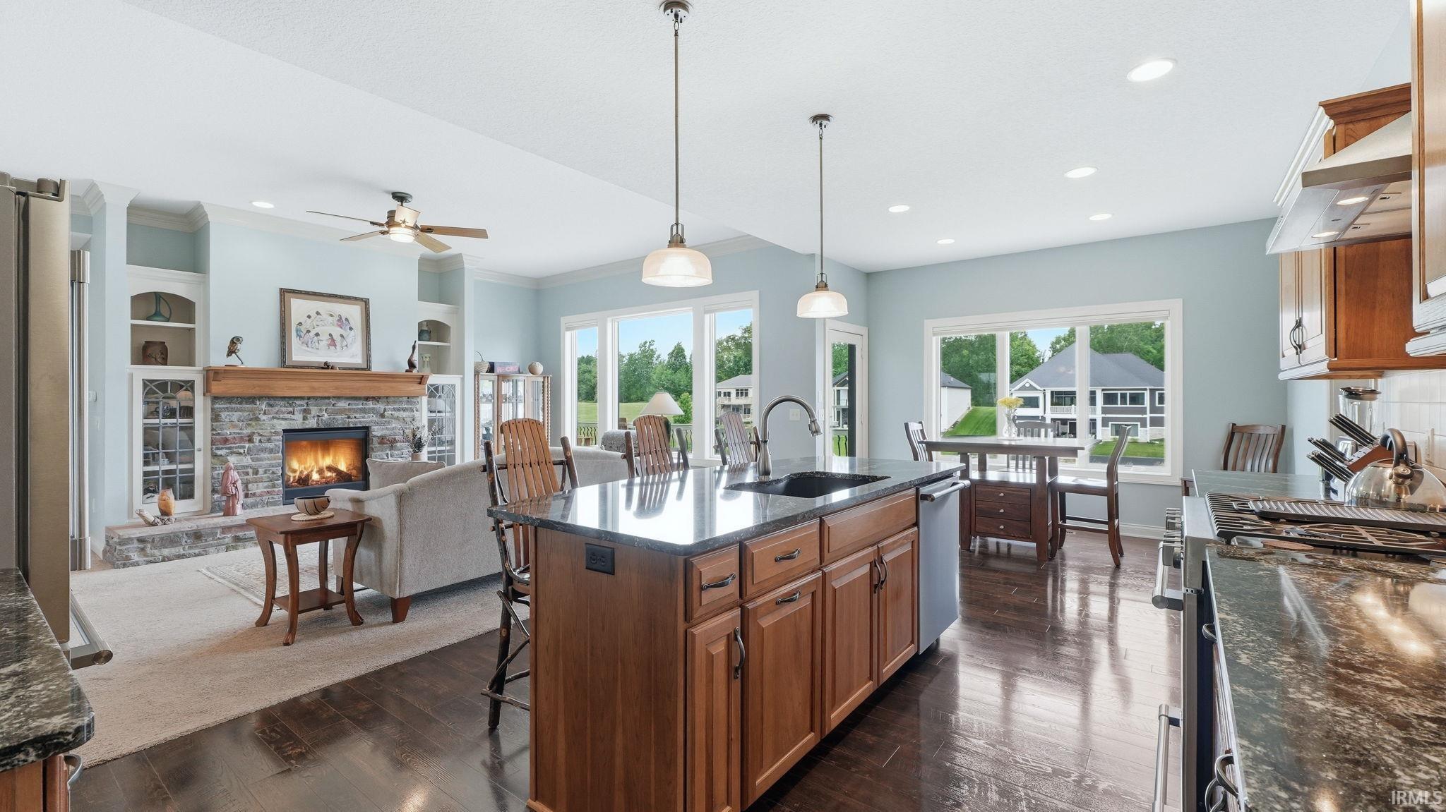 Open-concept living area featuring a kitchen island with seating, a stone fireplace, recessed lighting, and expansive windows