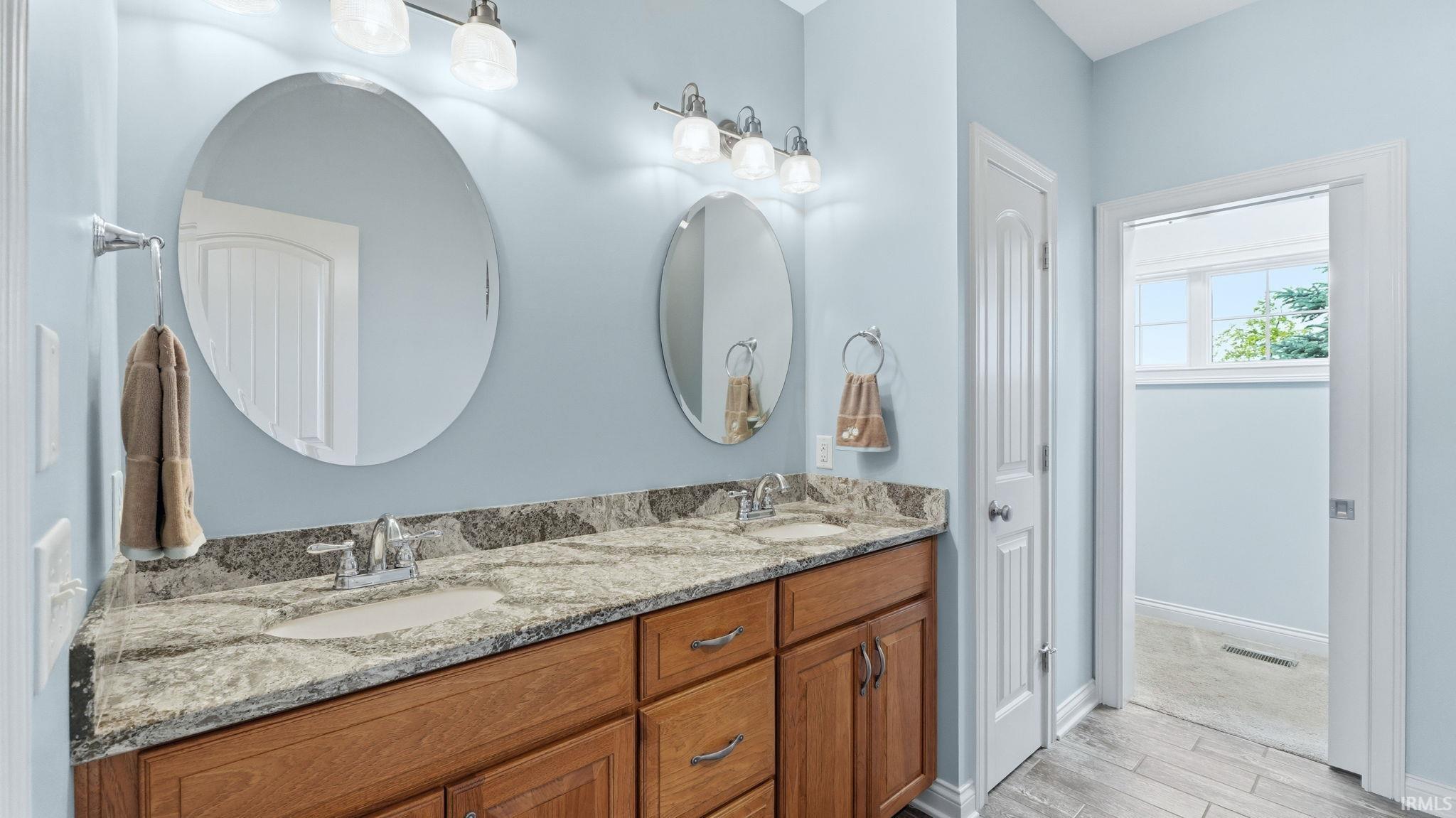 Dual vanity with wood-finish cabinetry, granite countertops, and under-mount sinks
