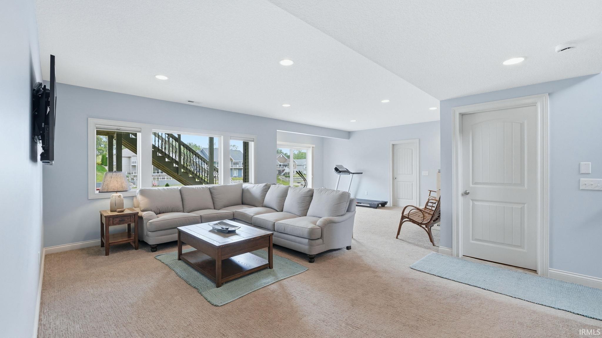 Spacious lower-level area with recessed lighting, light blue walls, and carpet flooring