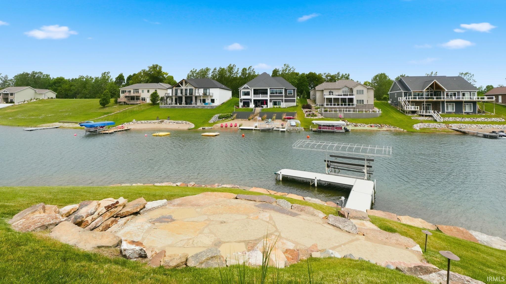 Expansive waterfront property featuring a private boat dock with lift system, sloped green lawn, and a stone patio