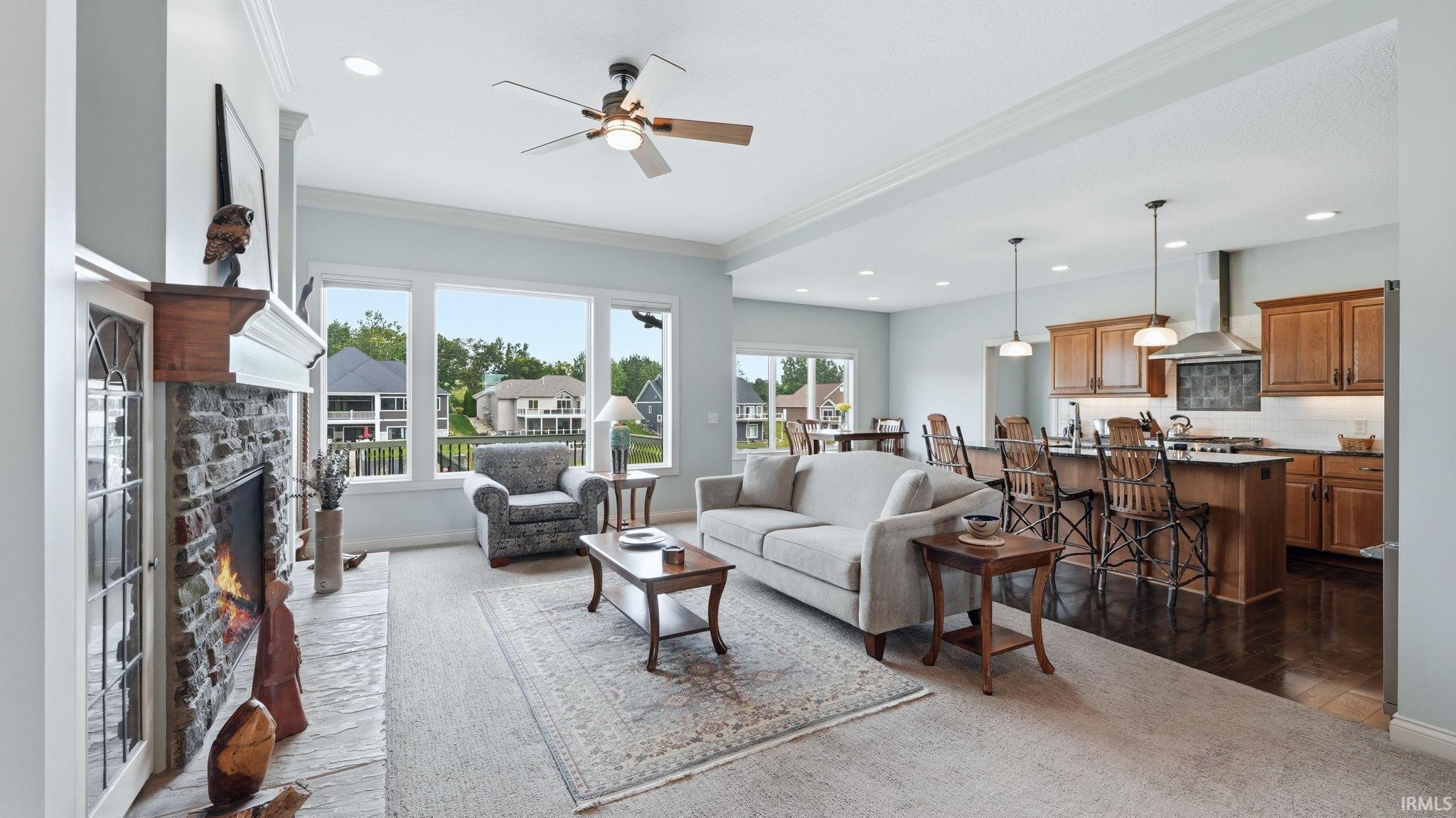 Open-concept living space featuring a stone fireplace with a substantial wood mantel, a ceiling fan with integrated lighting, recessed lighting, and expansive windows
