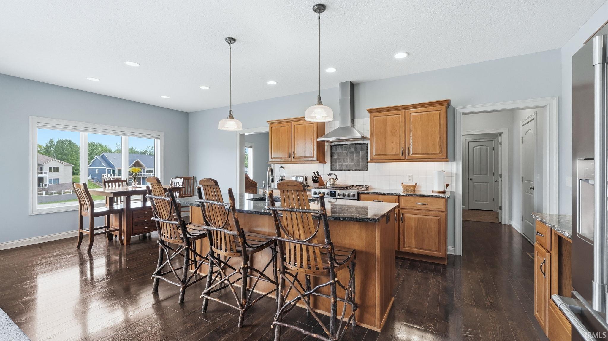 Open-concept kitchen featuring wood-finish flooring, a large center island with dark countertops, stainless steel appliances, and a dining area with expansive windows