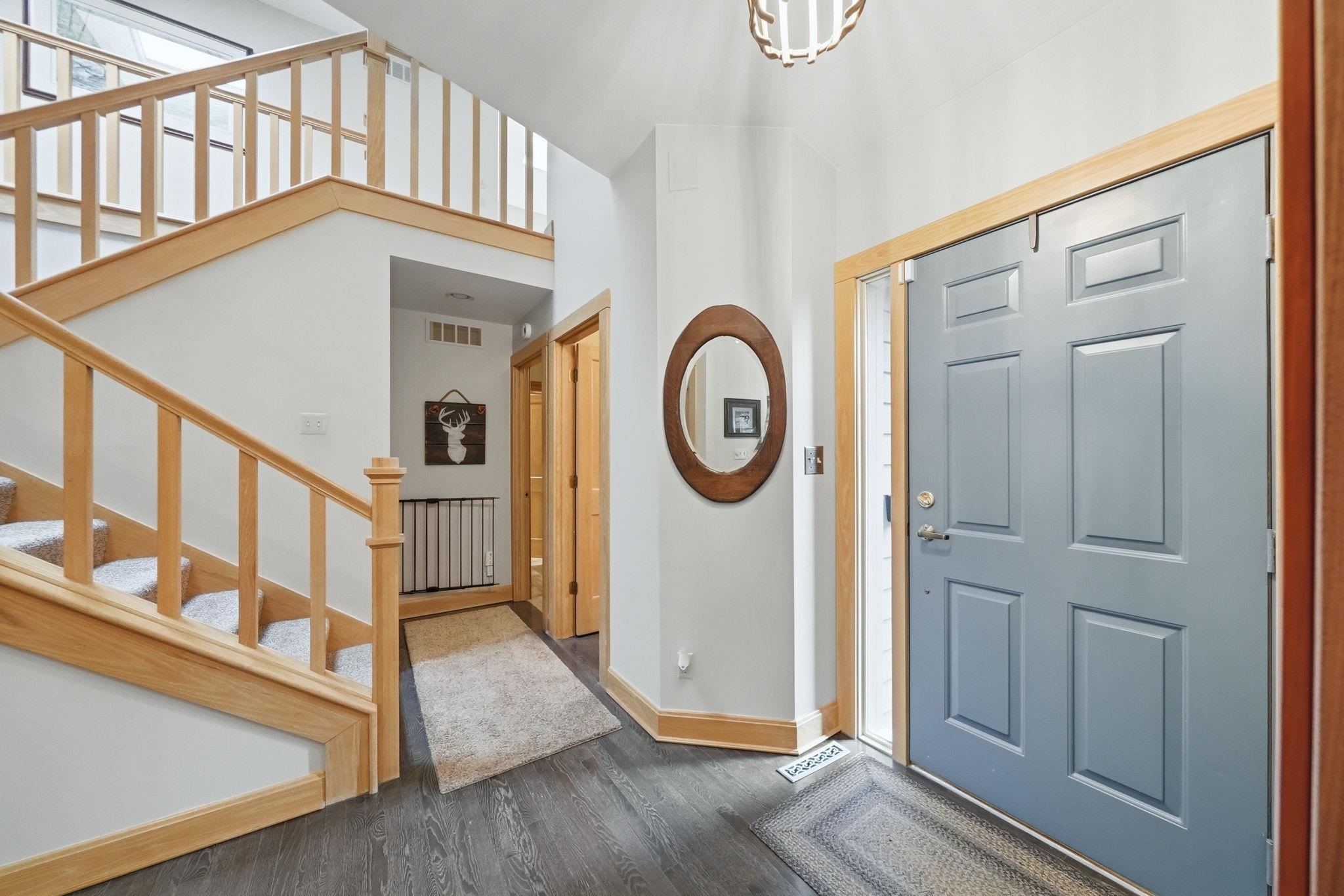 Entryway featuring a paneled front door, wood-finish flooring, a carpeted staircase with wood banisters, and natural wood trim throughout