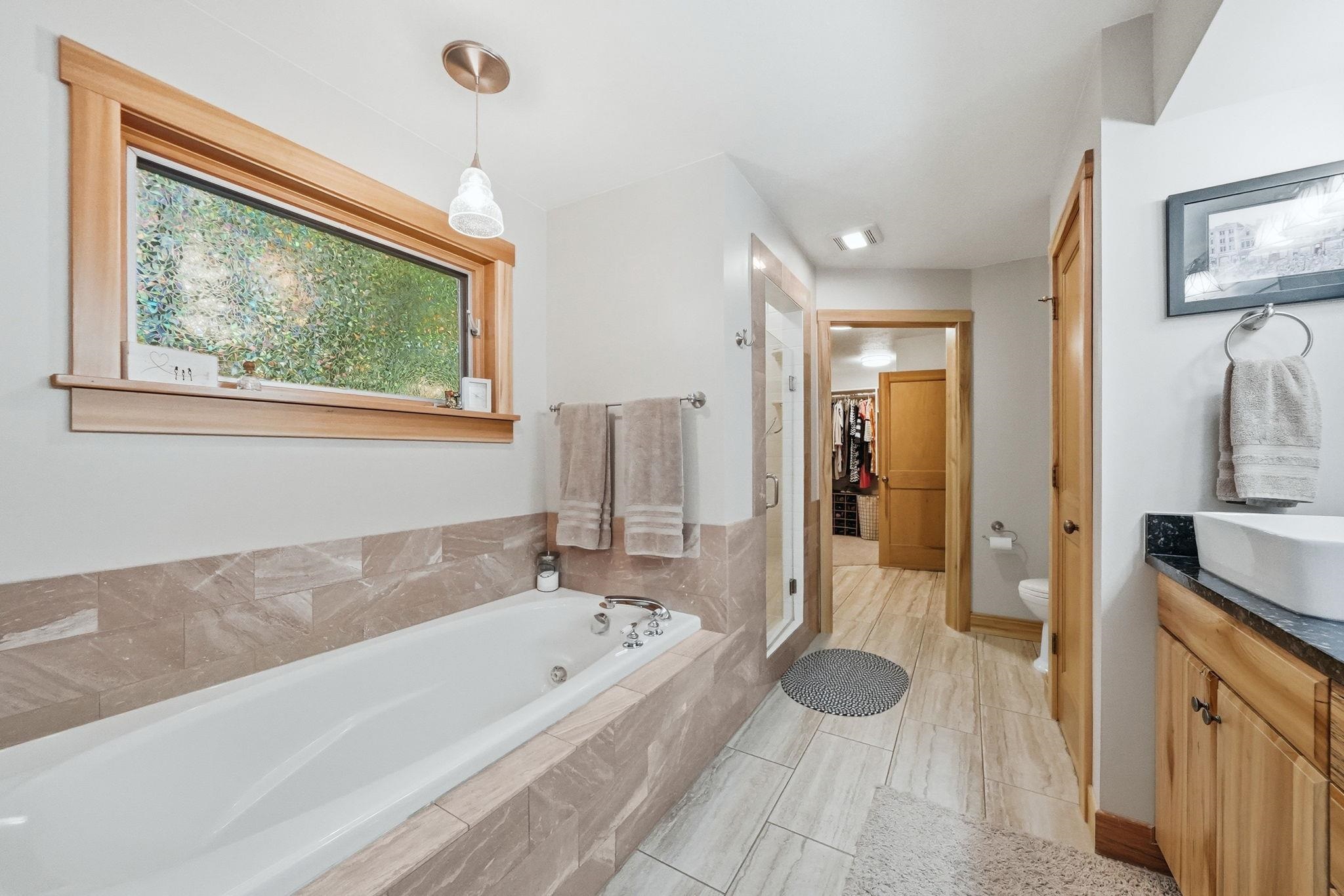 Built-in soaking tub with surrounding tilework and a wood-trimmed window