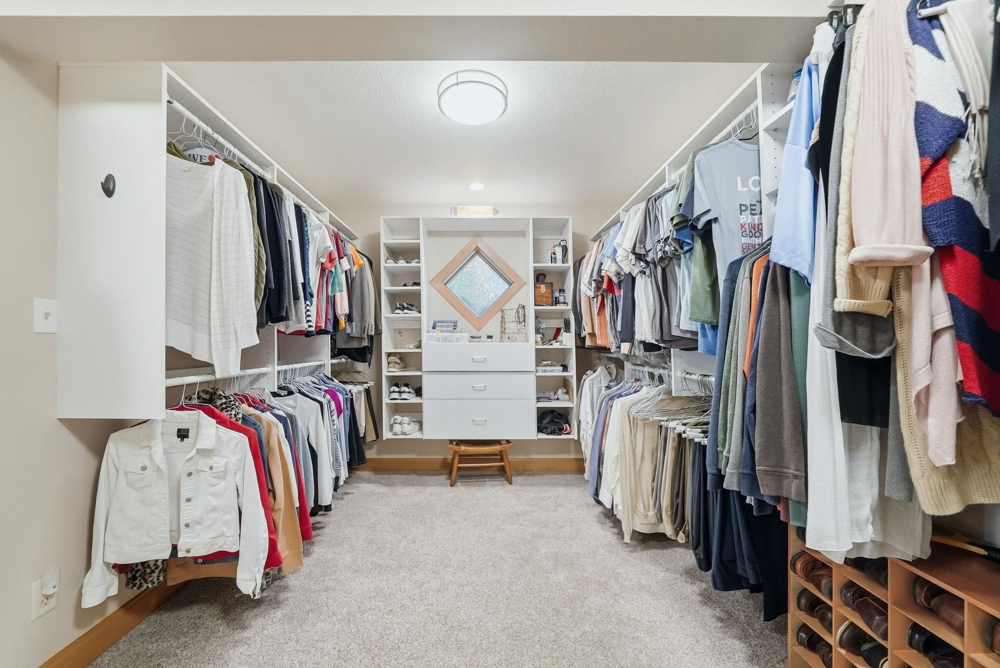 Expansive custom closet system featuring abundant hanging space, integrated shelving, central dresser with mirror, and carpeted flooring