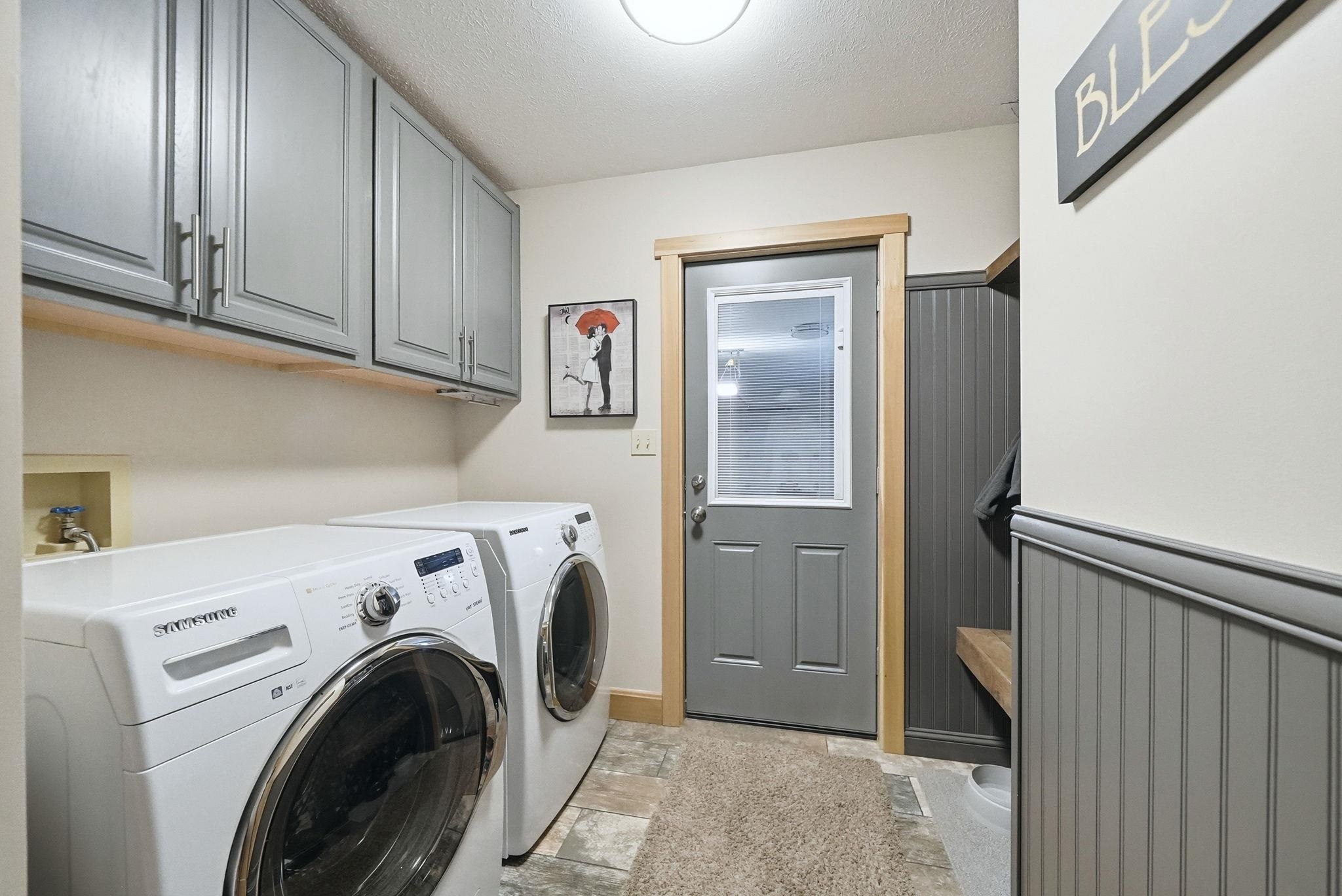 Dedicated laundry area featuring gray upper cabinetry with modern pulls, wood-finish shelving, and tiled flooring