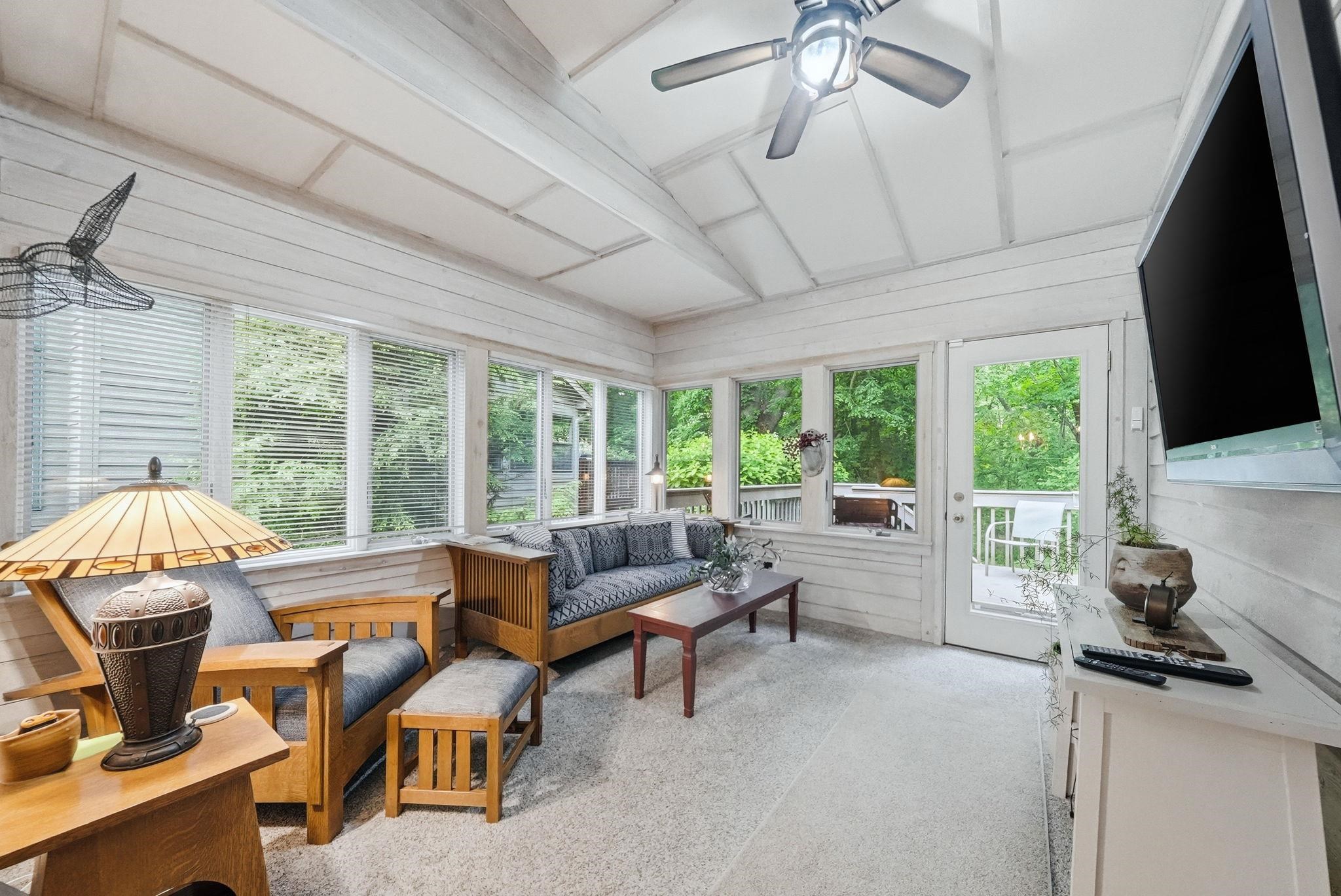 Enclosed porch featuring shiplap walls, a vaulted ceiling, multiple windows, and a glass-paneled exterior door leading to an outdoor deck