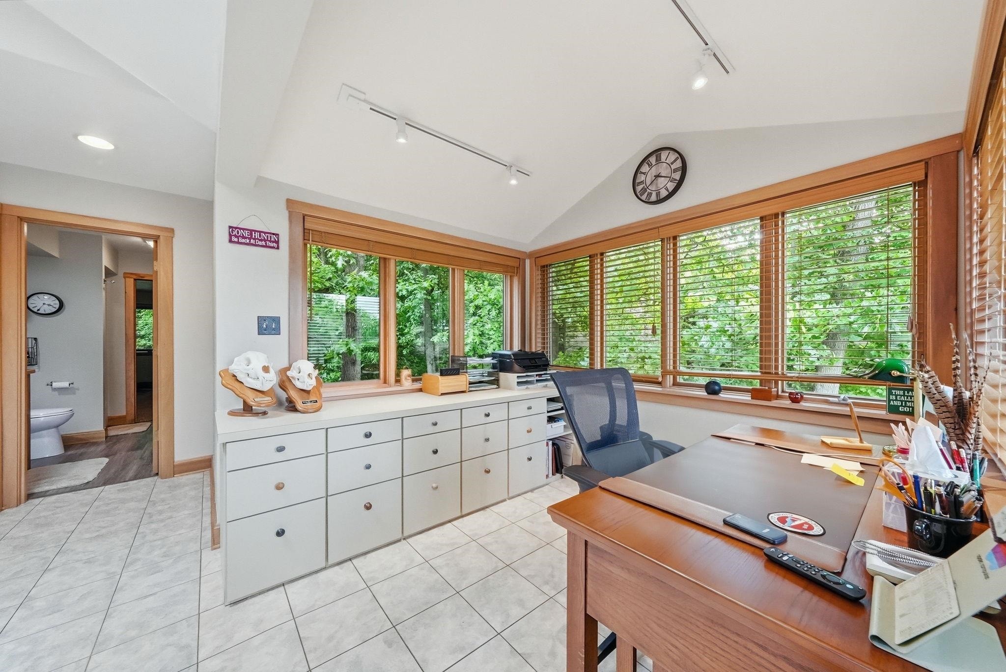 Bright workspace featuring extensive window trim, multiple windows with blinds, built-in lower cabinetry, vaulted ceilings, and track lighting
