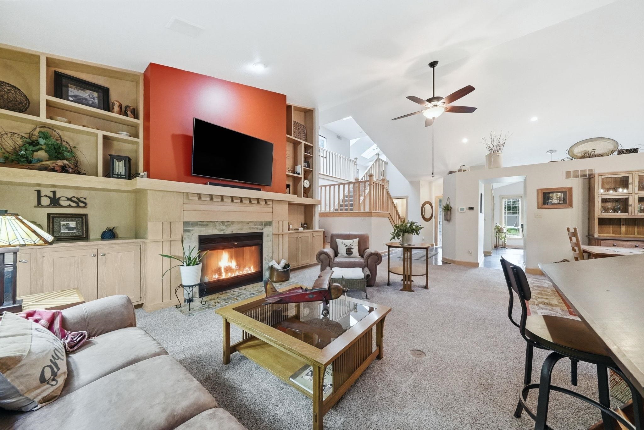 Living area featuring a fireplace with stone surround, custom built-in shelving, and a ceiling fan