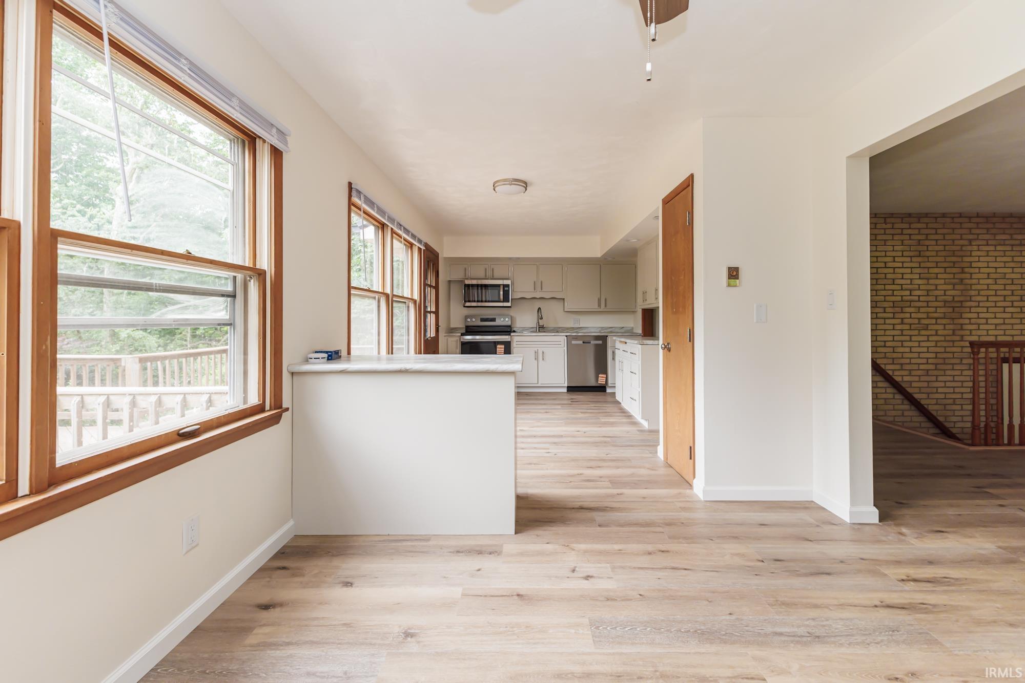 Open-concept living space with wood-finish flooring, a kitchen featuring light cabinetry and stainless steel appliances, and a breakfast bar with a light-toned countertop