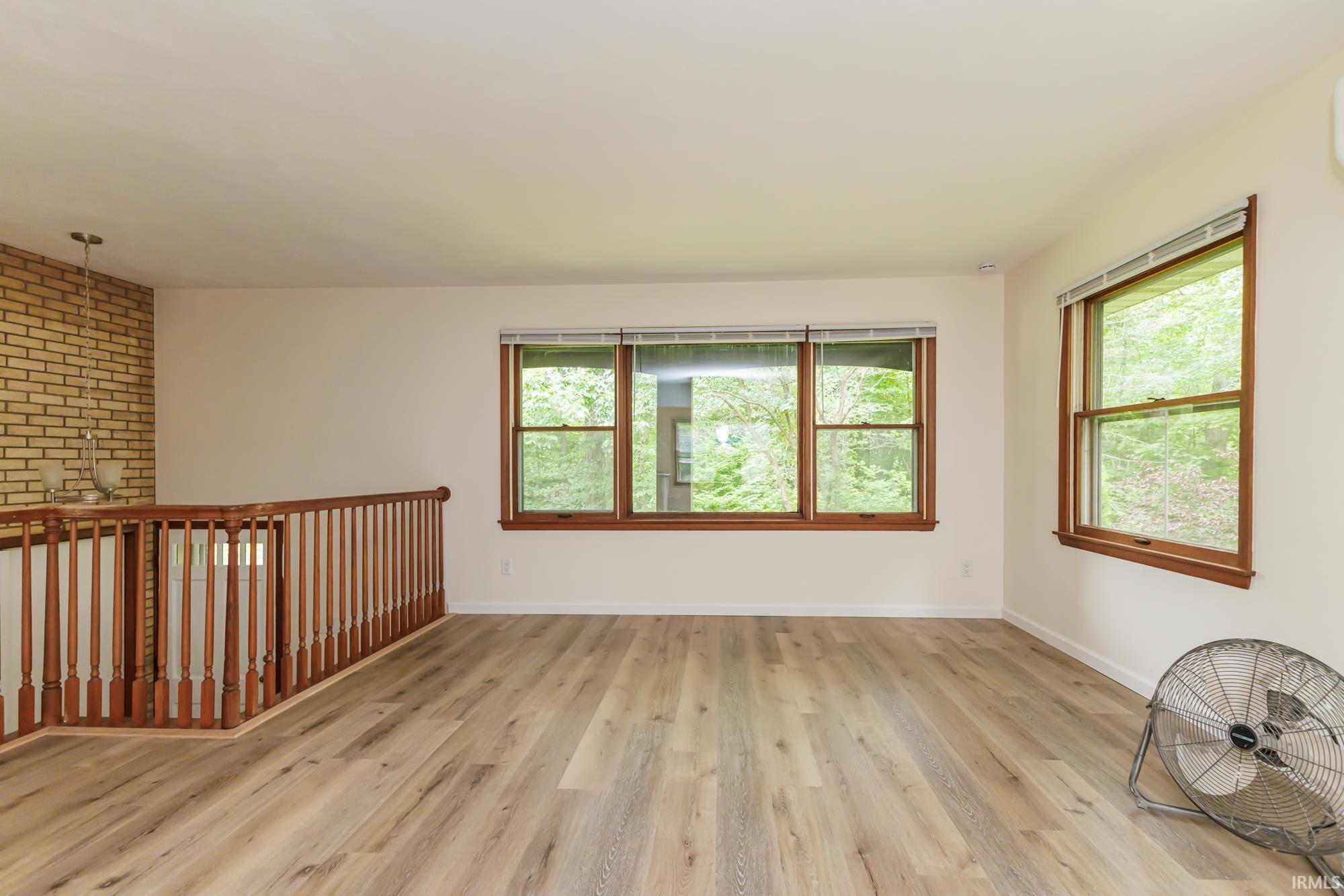 Spacious room featuring wood-finish flooring, light-colored walls, and multiple windows with wood trim