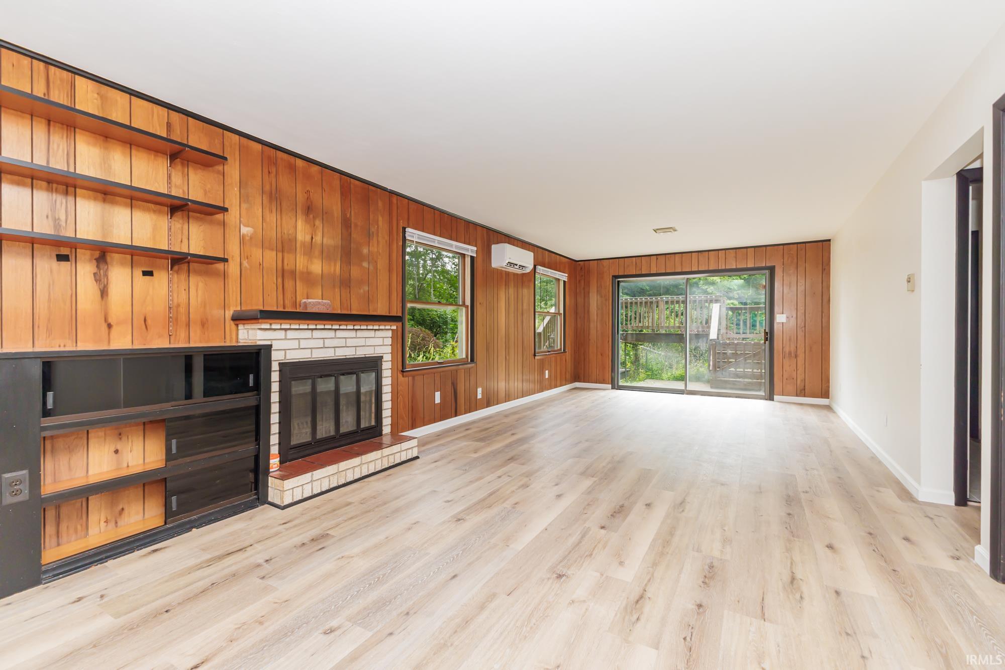 Spacious living area featuring wood-finish flooring, a brick fireplace, wood paneling, built-in shelving, and a sliding glass door