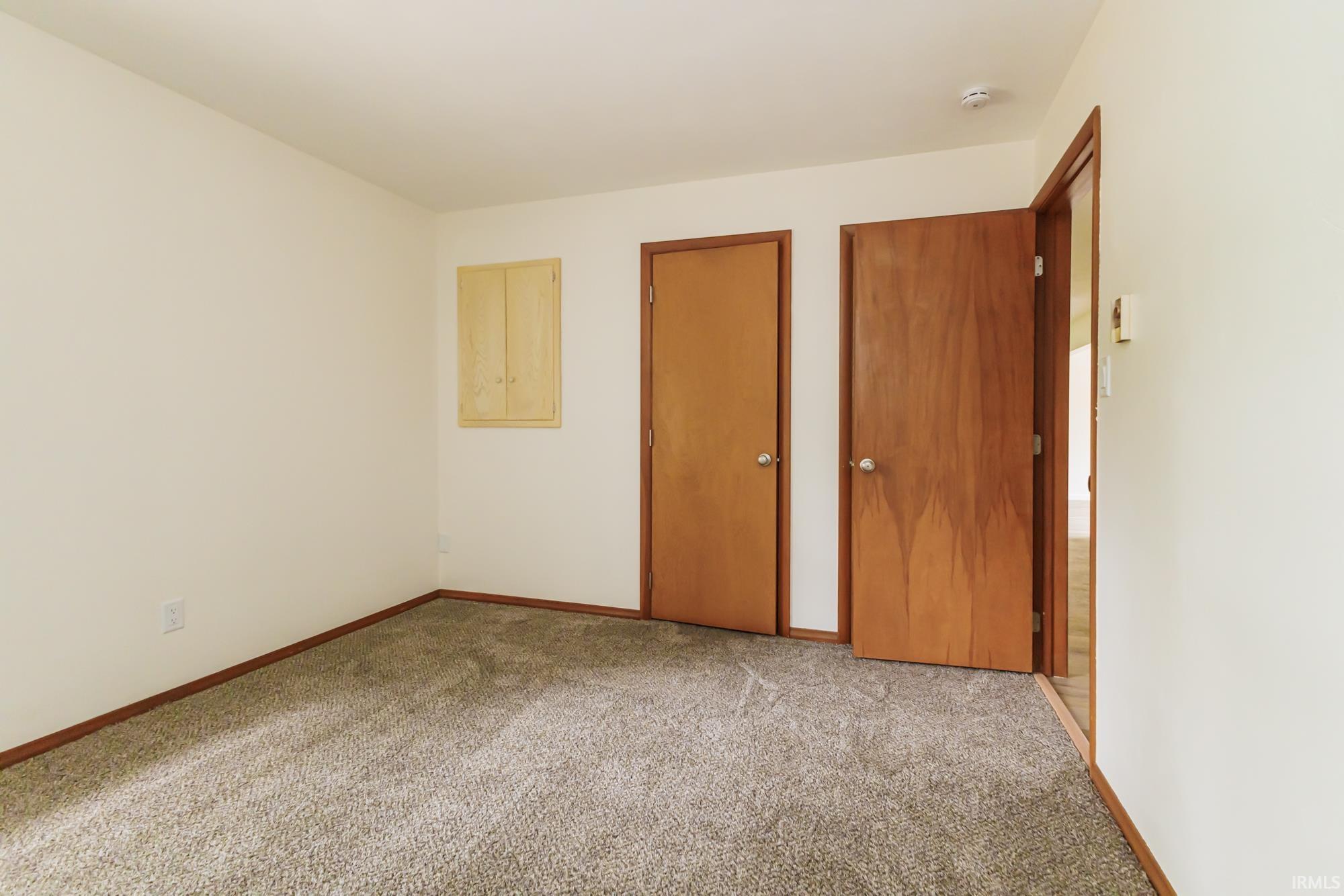 Carpeted interior space featuring two wood-finish doors, an integrated wall cabinet, white walls, and wood trim