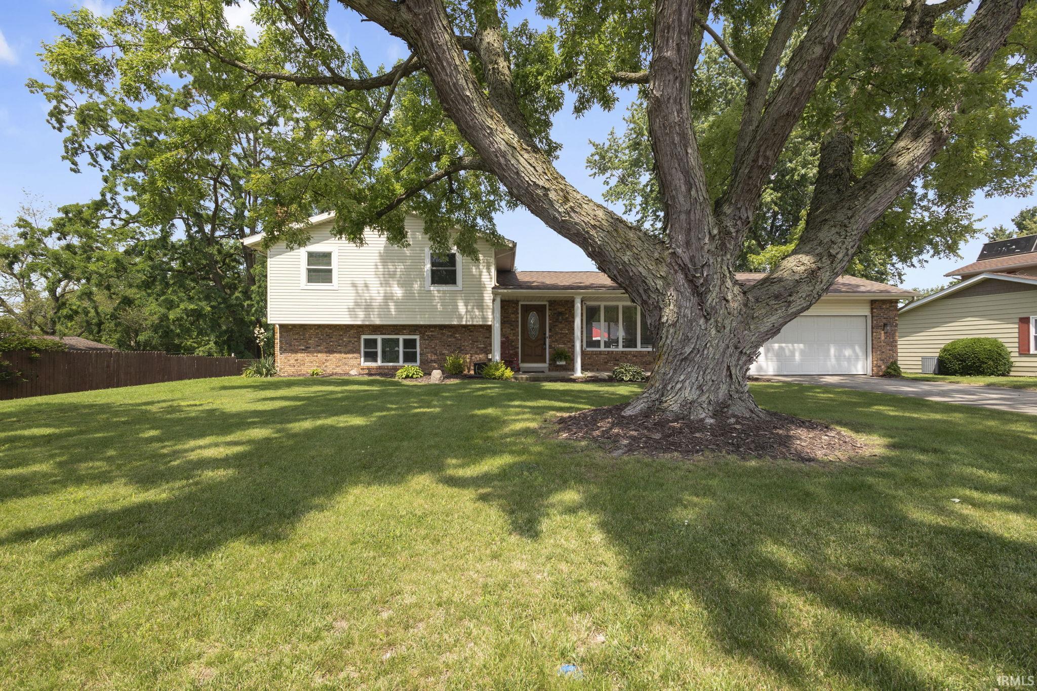 Split-level residence featuring brick and siding facade, a prominent mature tree, and an attached two-car garage