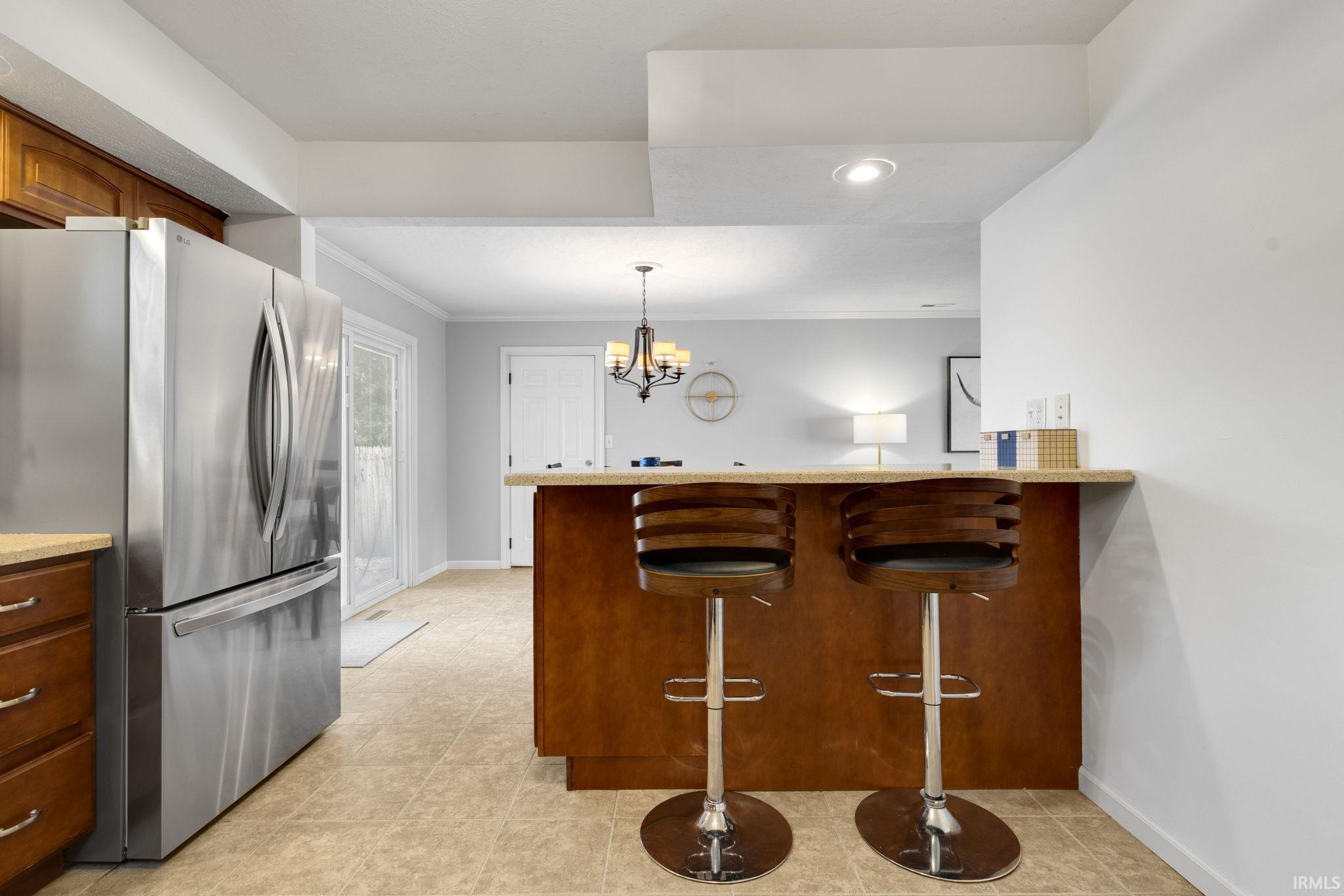 Breakfast bar with a stone-finish countertop and wood-finish base, stainless steel refrigerator, wood-finish cabinetry, and light-colored tile flooring