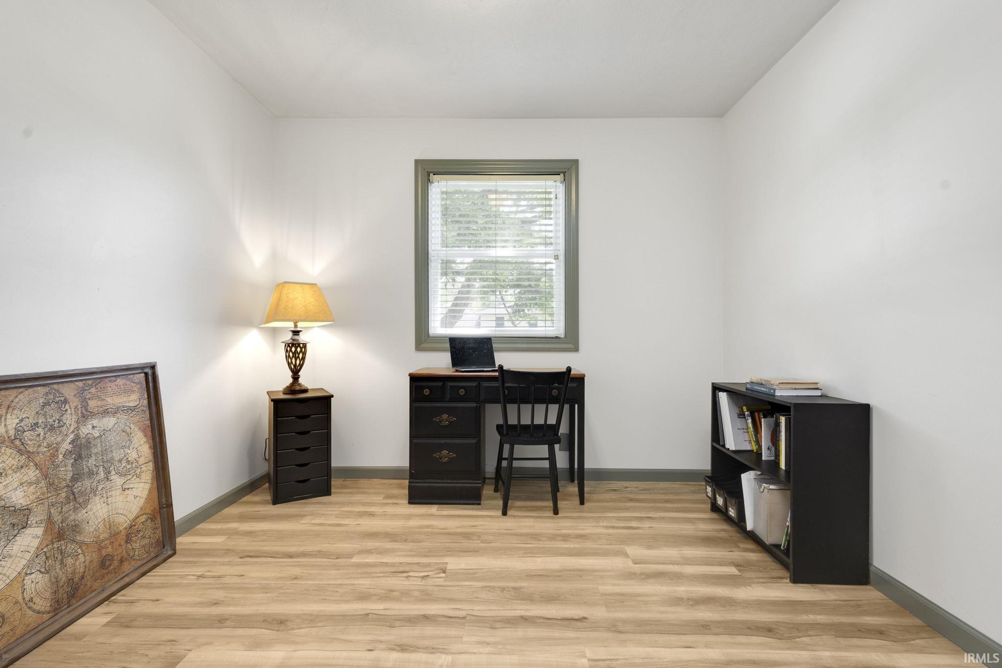Bright room featuring light wood-finish flooring, white walls, and a window with blinds