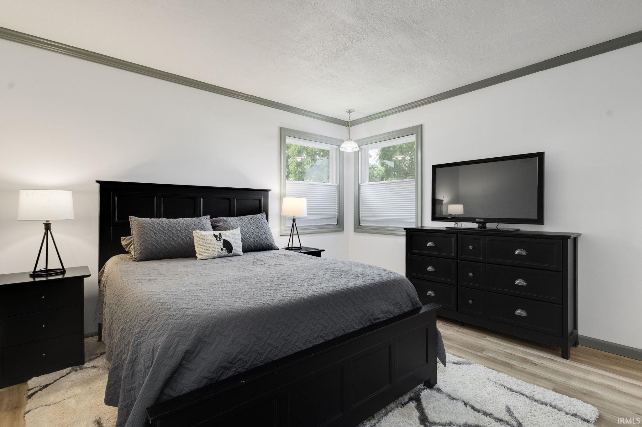Room featuring wood-finish flooring, two large windows with blinds, and white walls complemented by dark trim molding