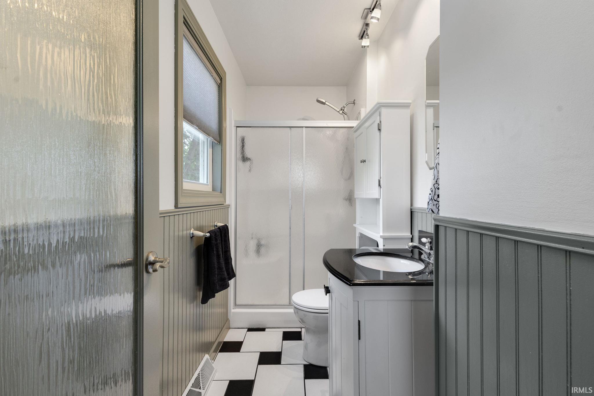 Bathroom featuring a black and white checkered tile floor, beadboard wainscoting, and a white vanity with a dark countertop