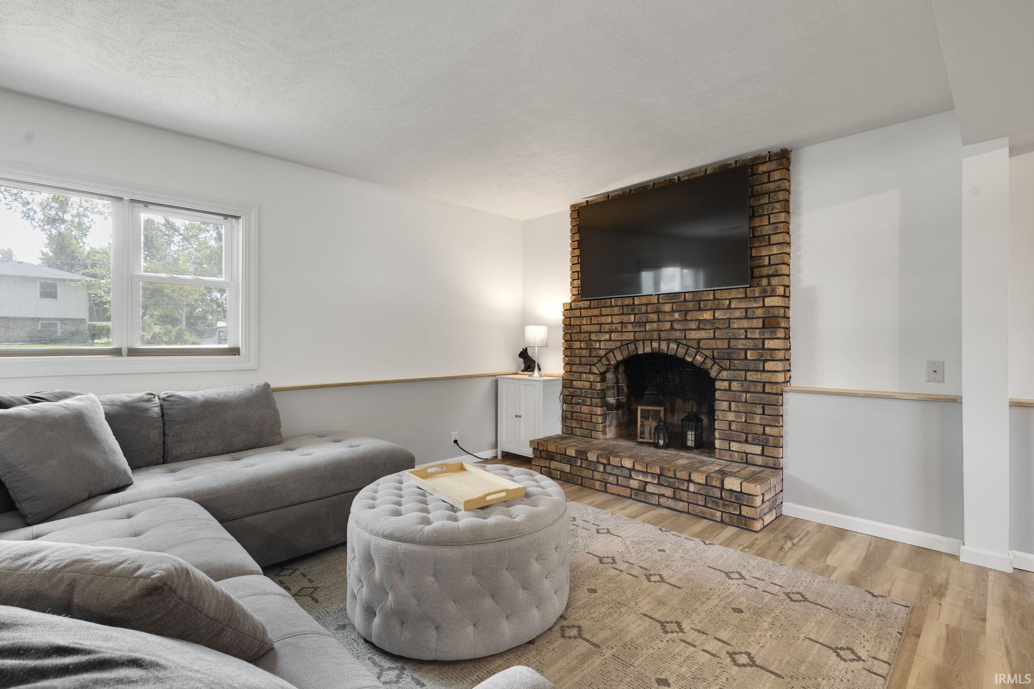 Living area featuring a brick fireplace with an arched opening, wood-finish flooring, and white walls with a light-toned chair rail