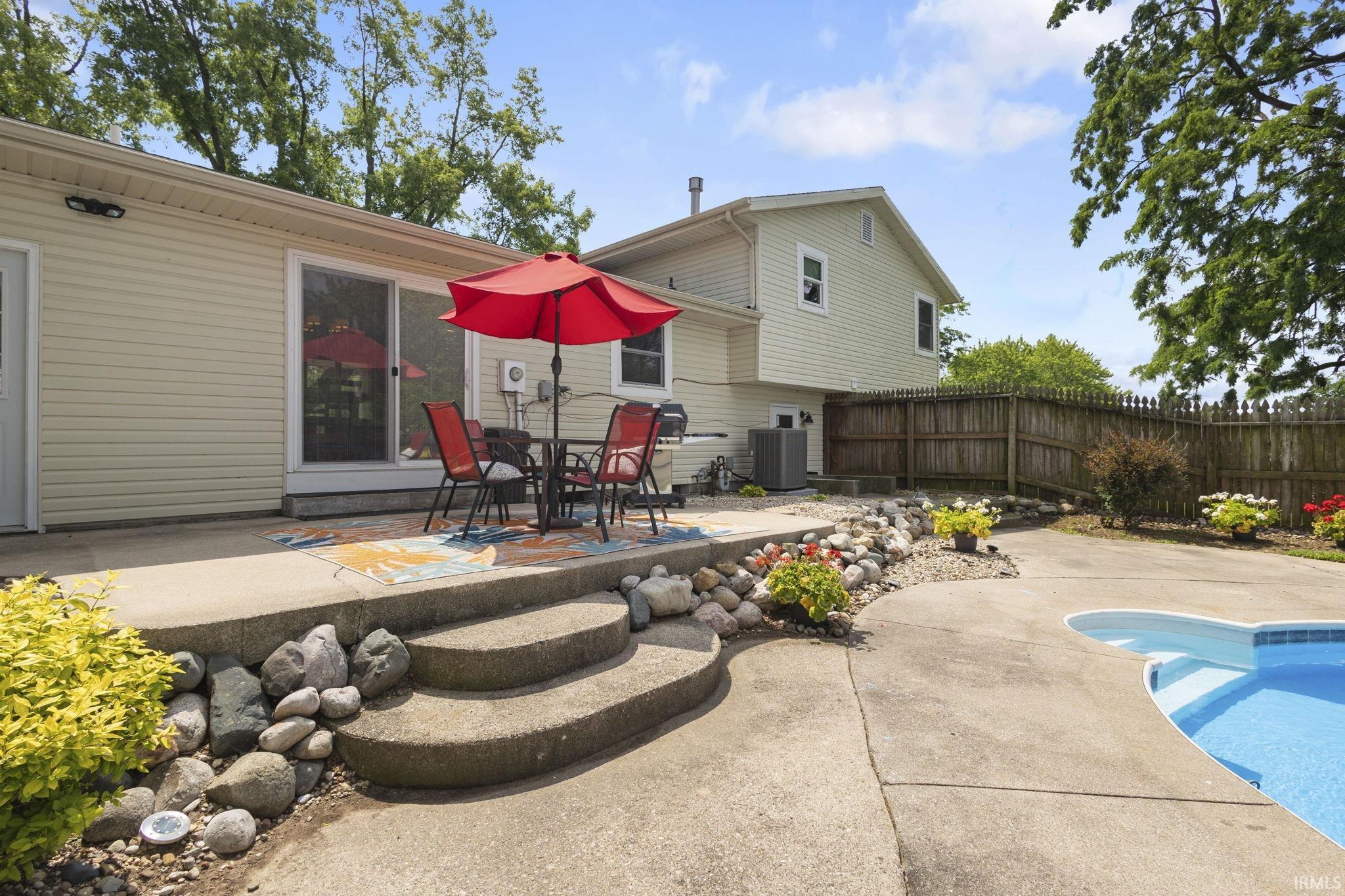 Outdoor entertaining area featuring a concrete patio with curved steps, a rock garden, and a built-in swimming pool
