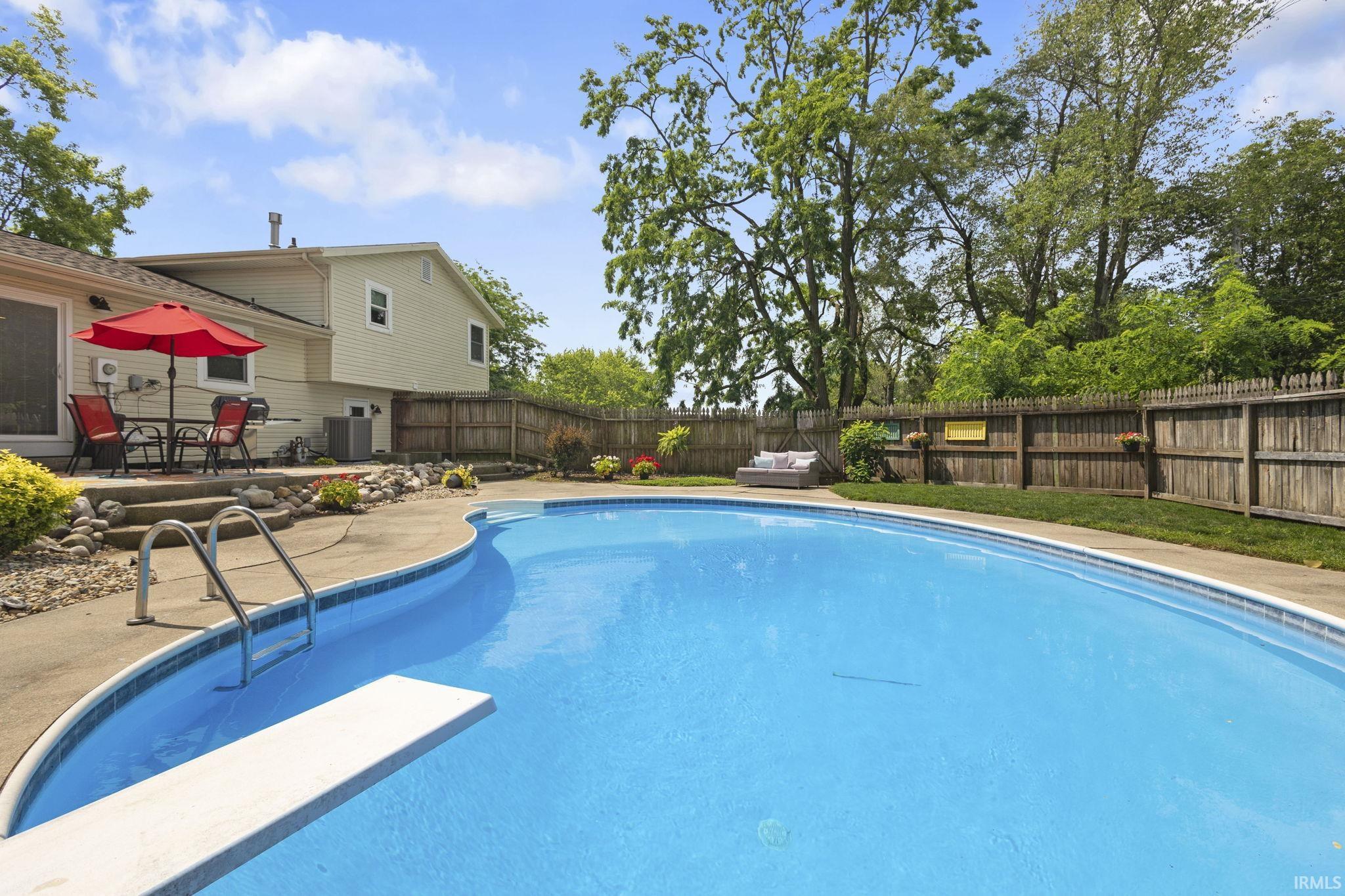 Fenced backyard featuring a large swimming pool with a diving board, concrete surround, and direct access to a patio