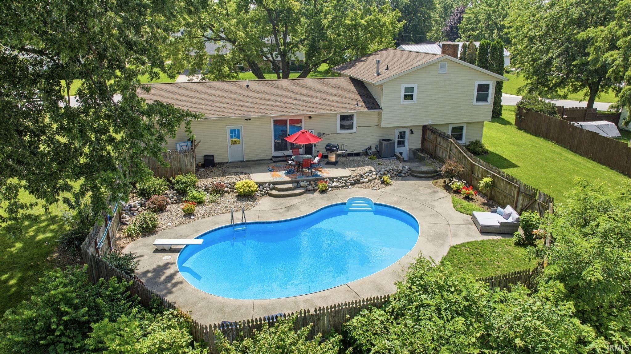 Rear exterior featuring a large in-ground swimming pool, concrete patio, and mature landscaping