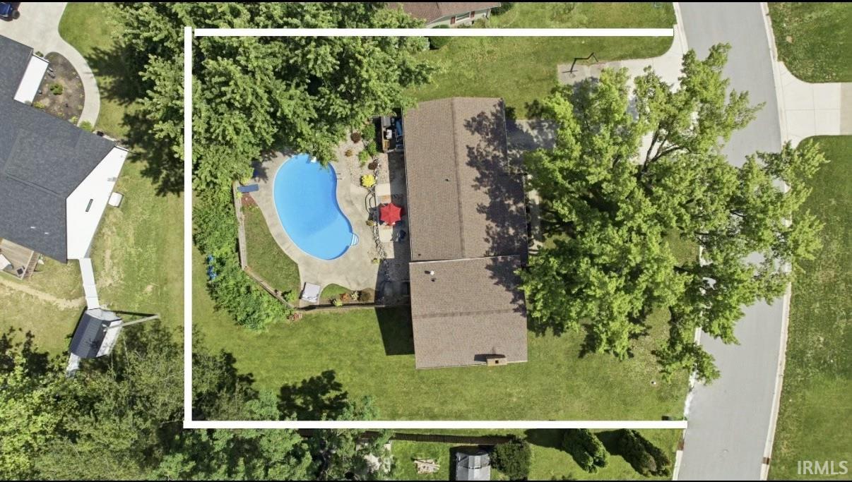 Expansive property featuring a freeform in-ground pool, surrounding concrete patio, mature trees, and a substantial grassy lawn