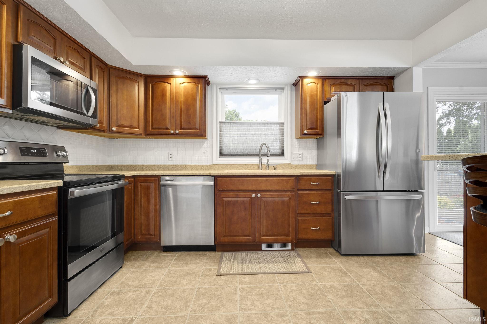 Kitchen featuring wood cabinetry, stainless steel appliances, light-toned countertops, and a tiled floor