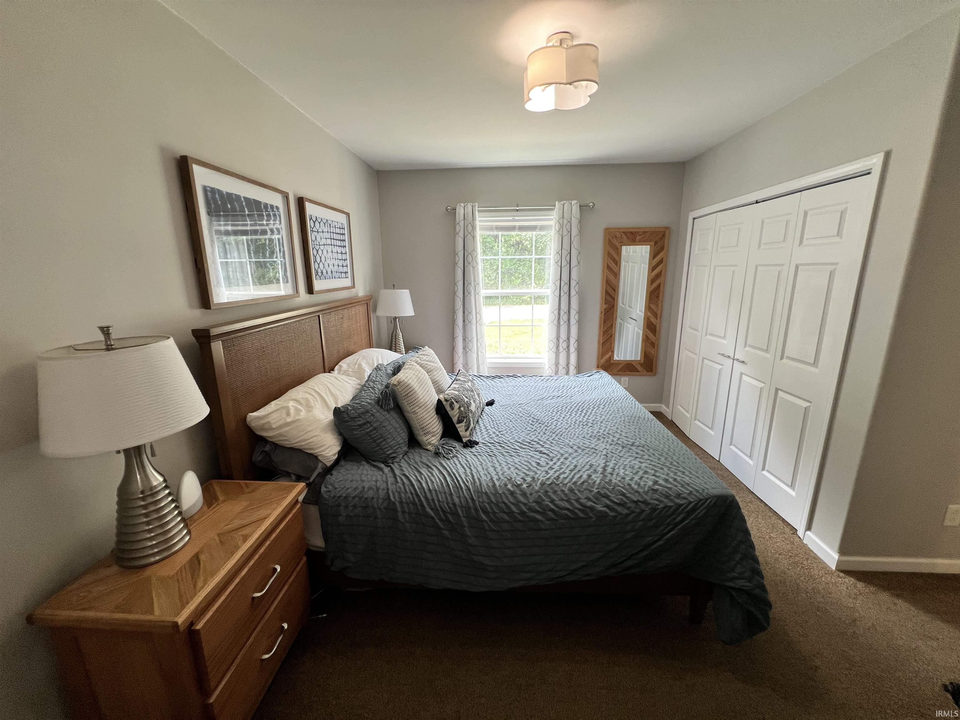 Bedroom featuring a window with patterned drapes, a flush-mount ceiling light fixture, and textured carpeting