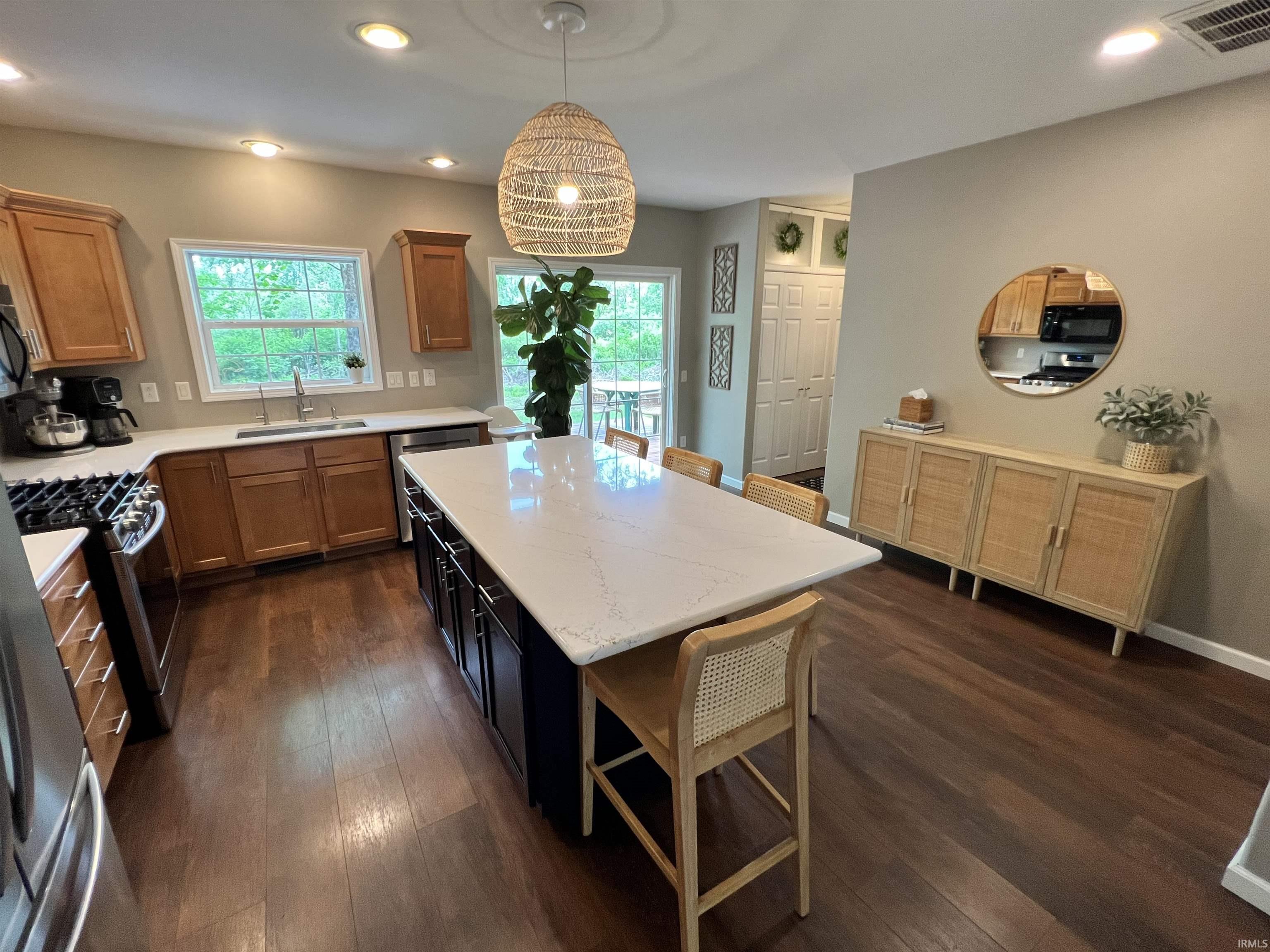 Kitchen featuring a large central island with a light-toned countertop, stainless steel appliances, wood-finish flooring, and light-stained cabinetry