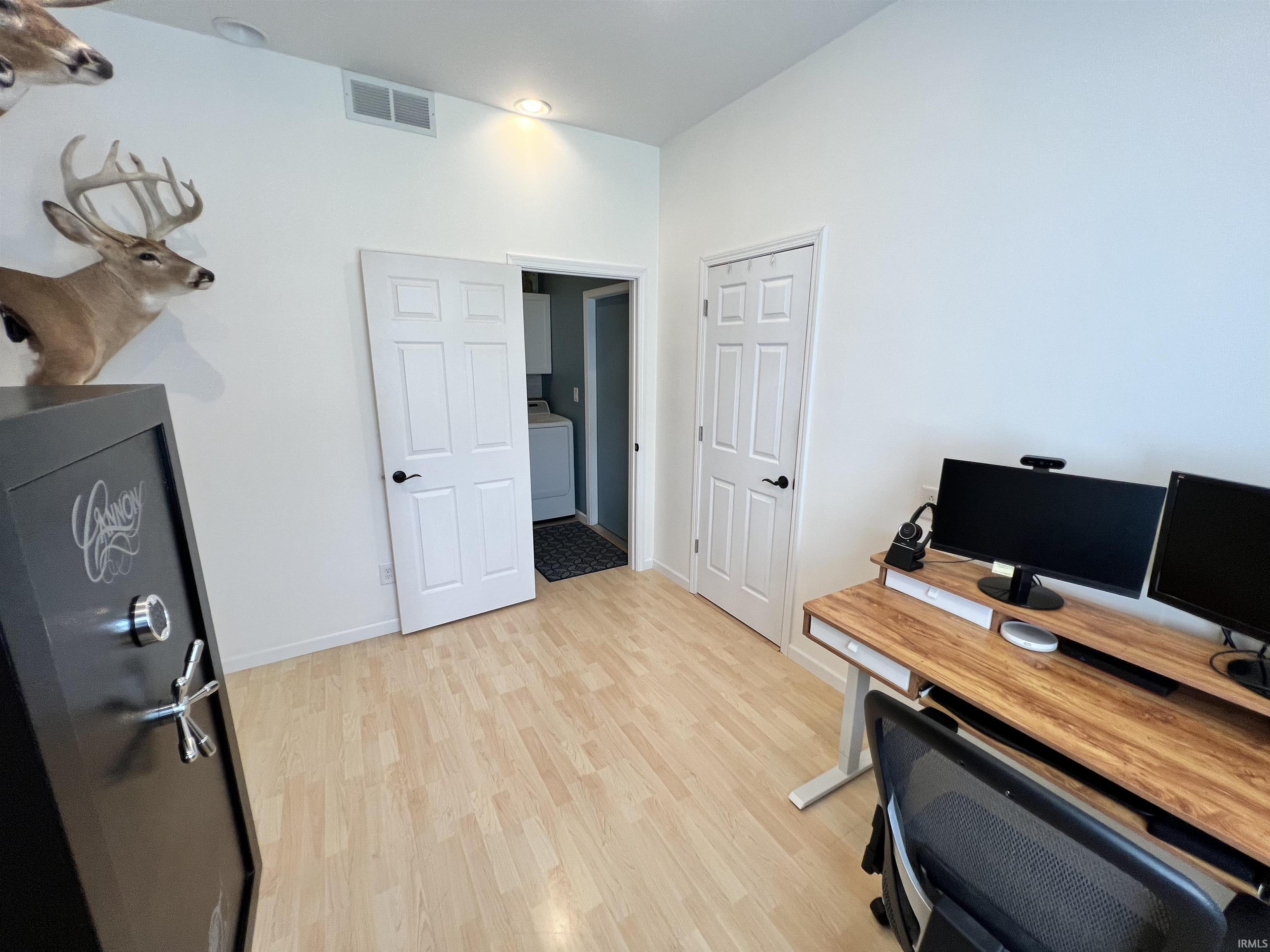 Room featuring wood-finish flooring, two six-panel doors with black hardware, and an exposed laundry area with a washer and dryer