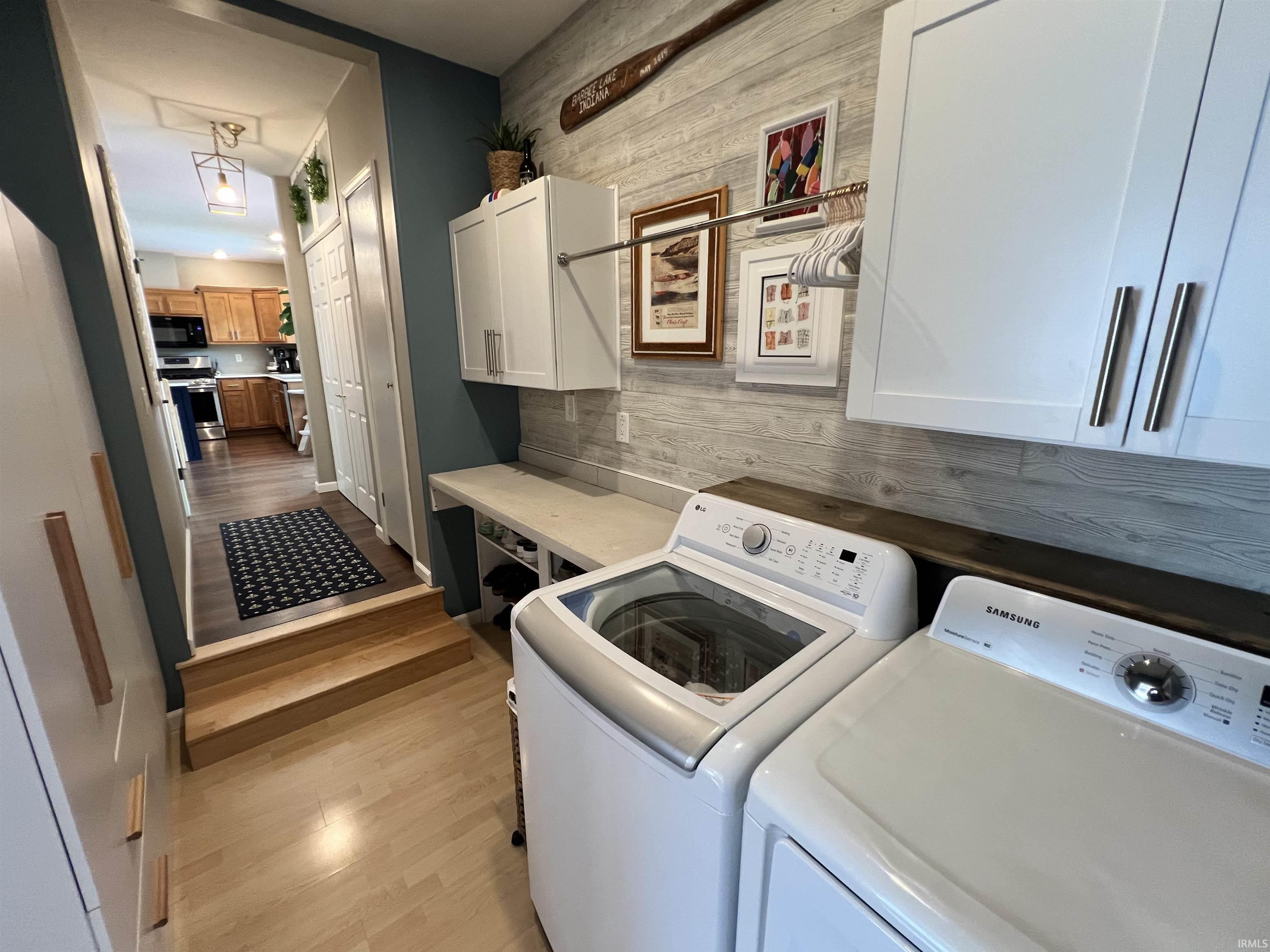 Dedicated laundry area featuring white cabinetry, light wood-finish flooring, and a wood-paneled accent wall