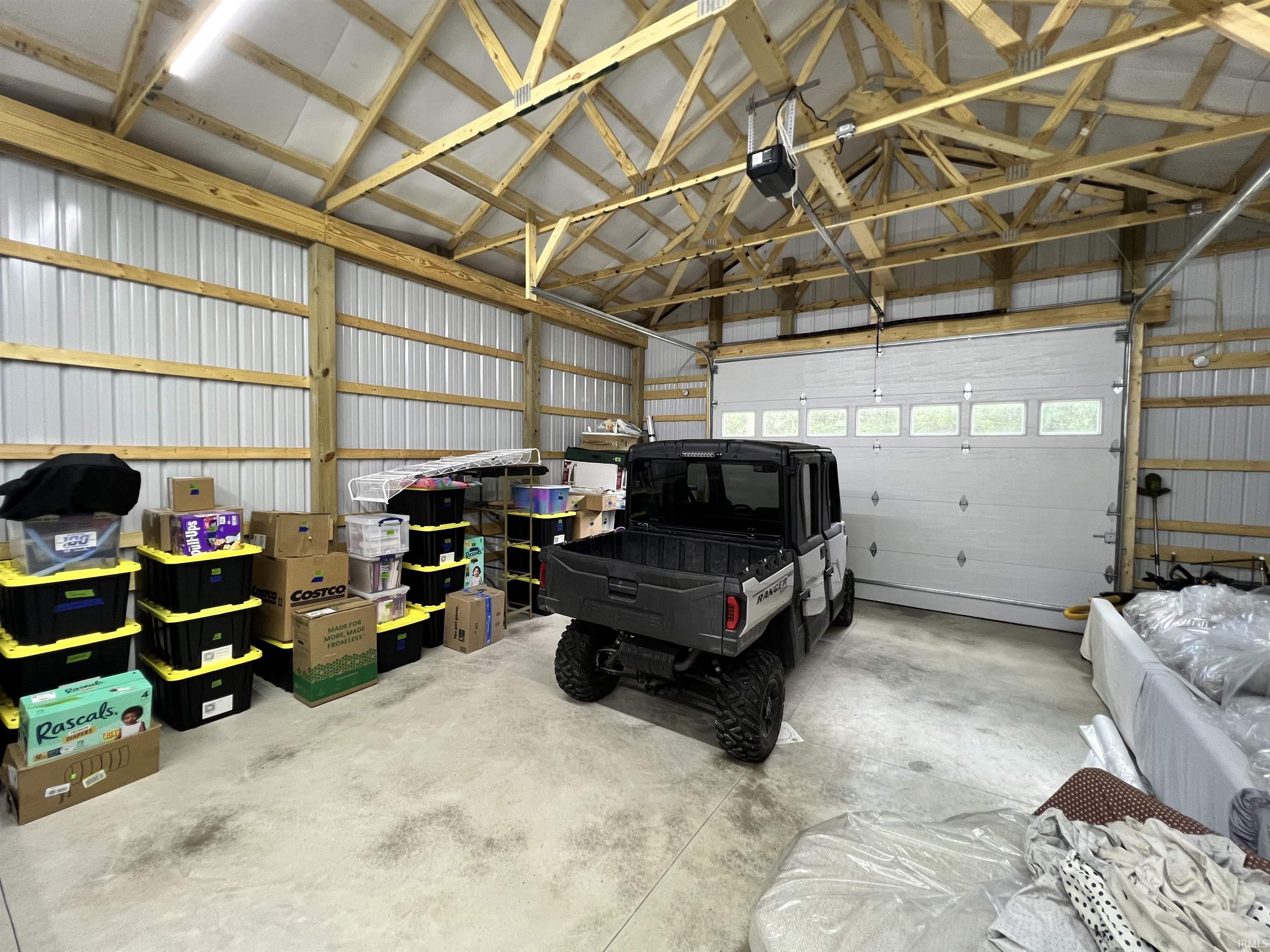 Spacious outbuilding featuring a concrete floor, exposed wooden rafters, 12 foot Ceilings, corrugated metal walls, overhead lighting, and an automatic garage door with window panels
