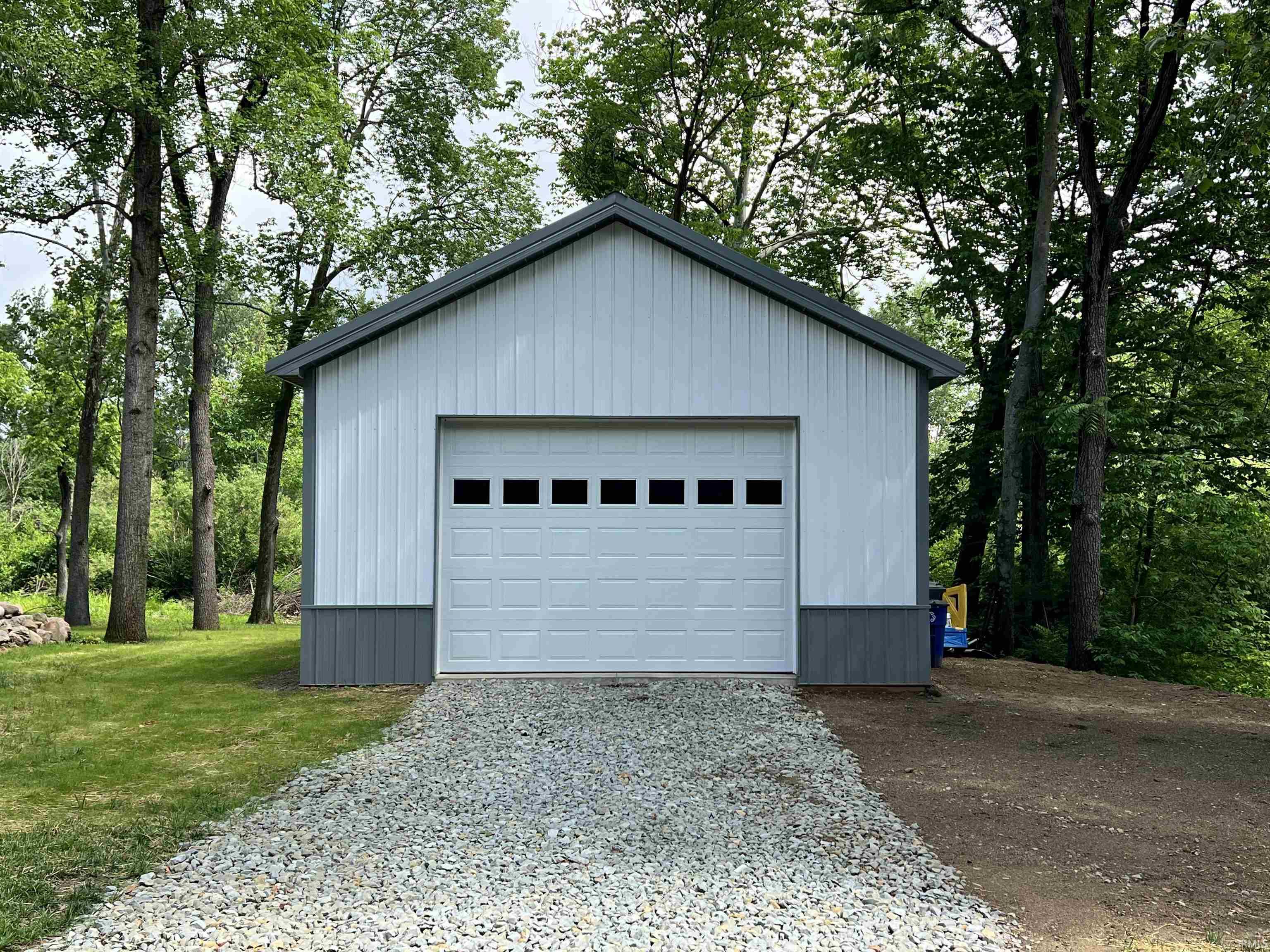 Pole Building featuring vertical siding, a gray metal roof, and a panel garage door with upper-row windows