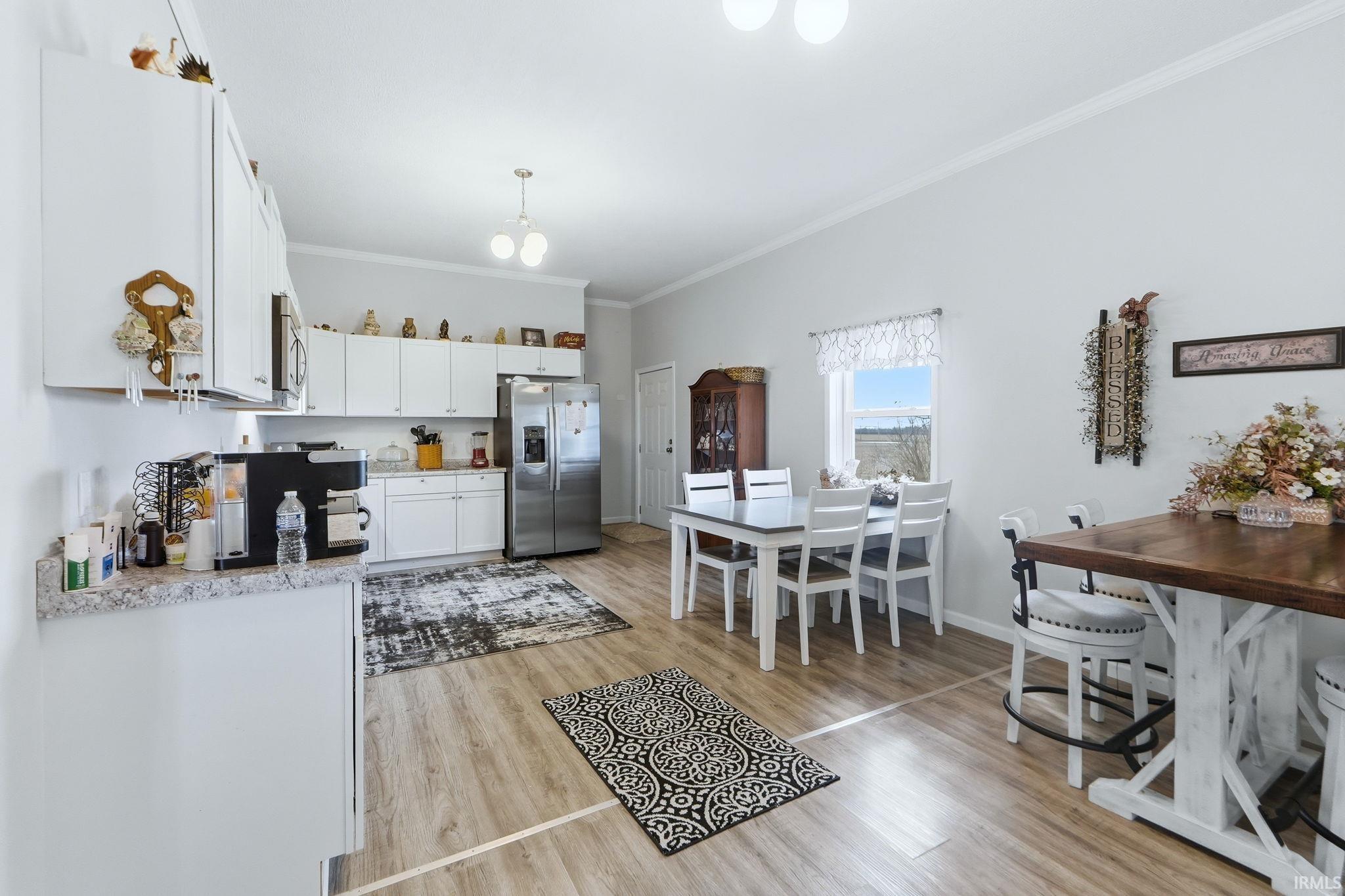 Open-concept kitchen and dining area featuring wood-finish flooring, white cabinetry, light-toned countertops, a stainless steel refrigerator, and crown molding