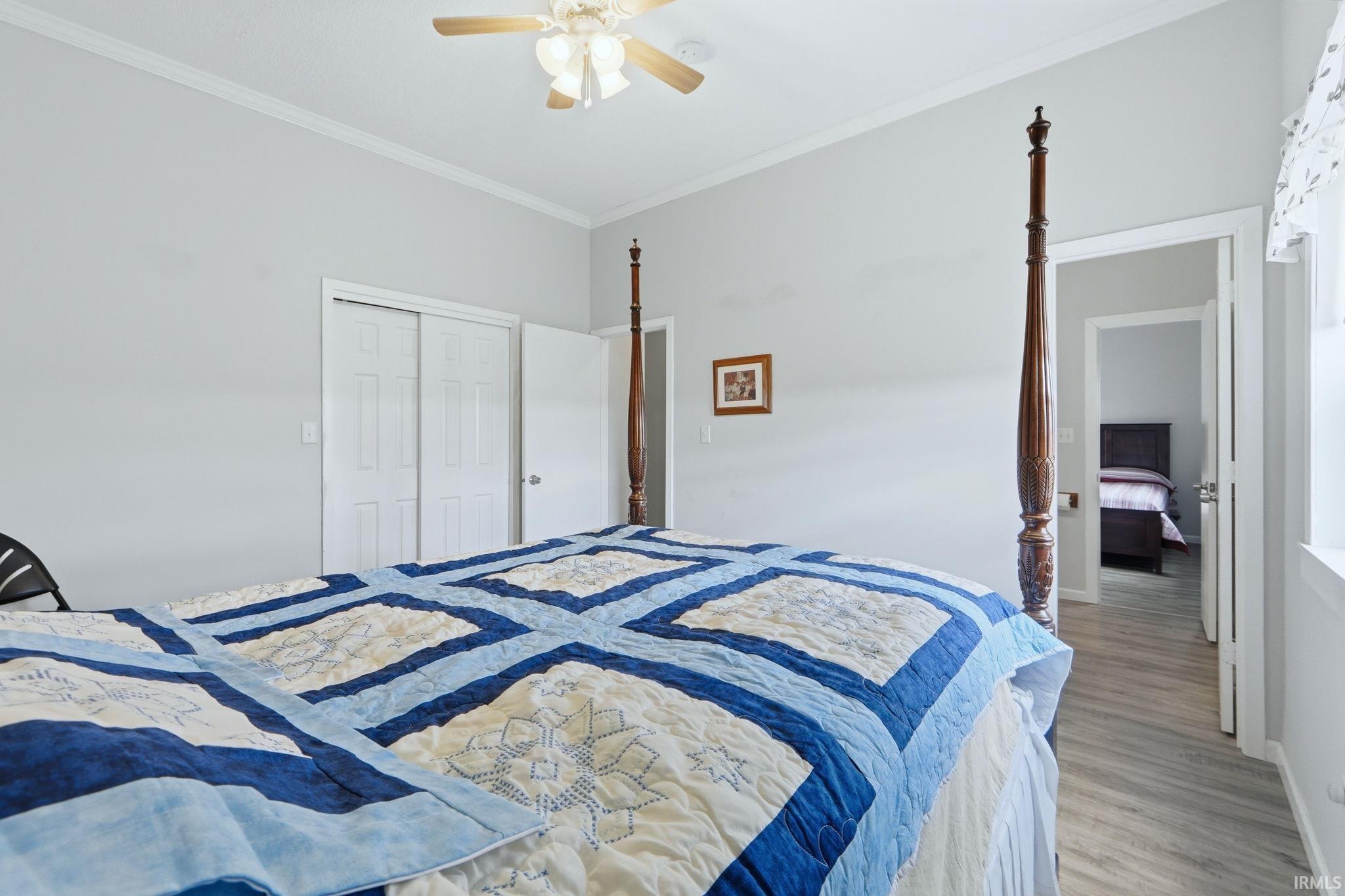 Bedroom featuring wood-finish flooring, a ceiling fan with integrated lighting, white trim, and a double-door closet