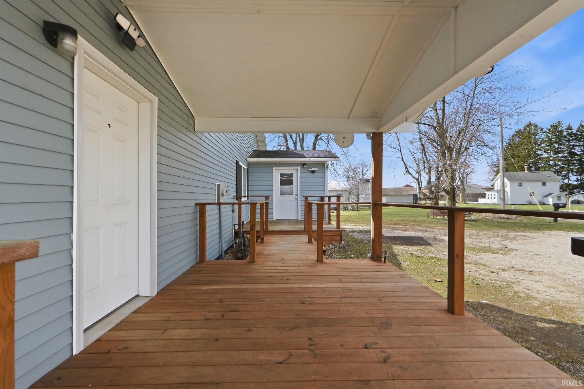Expansive covered wood-finish deck with wooden railings, light blue siding exterior, and exterior lighting fixtures